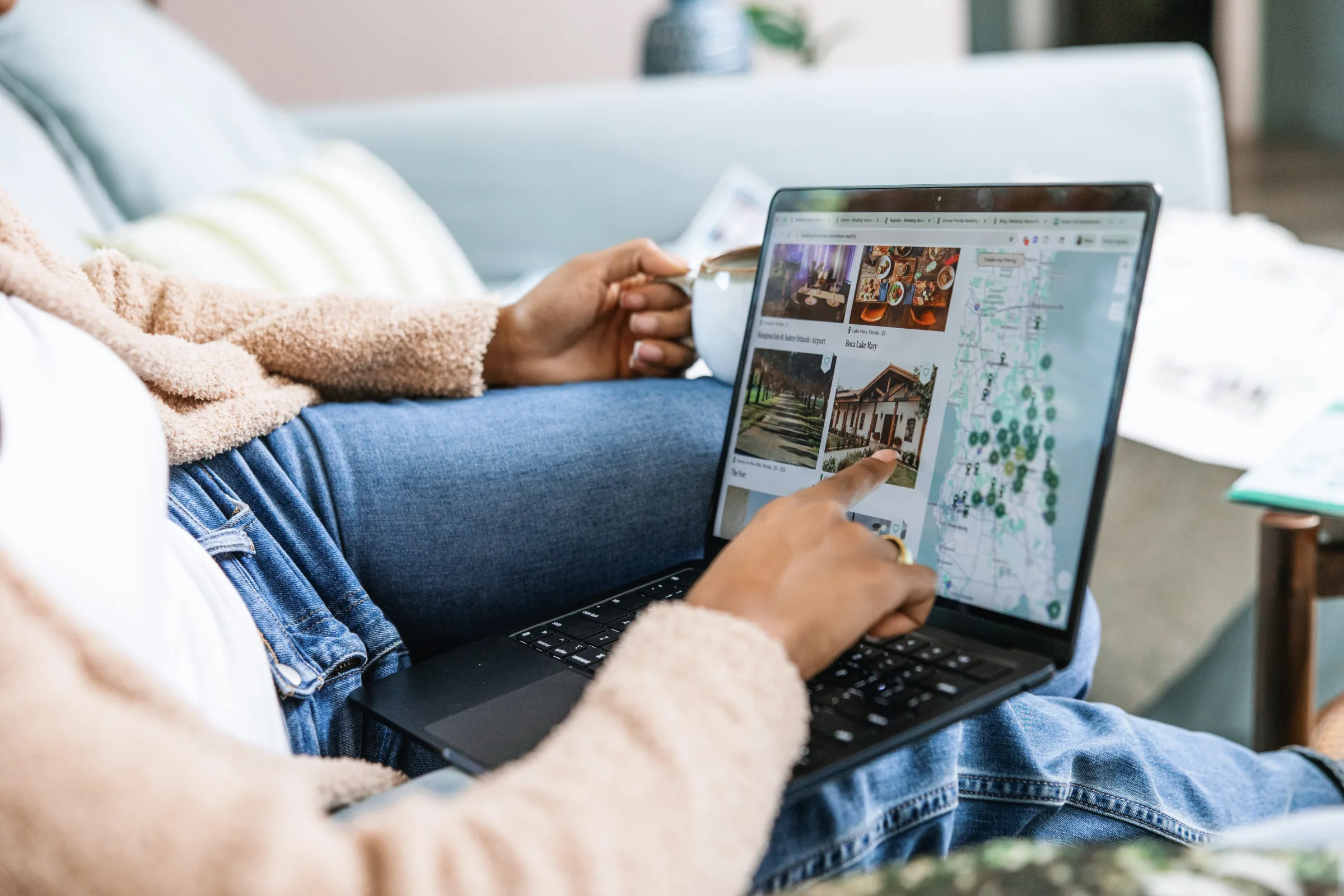 Newly engaged couple sitting on a couch with a laptop open to Wedding Venue Map on their lap. Searching for venues and pointing at the screen at a venue.