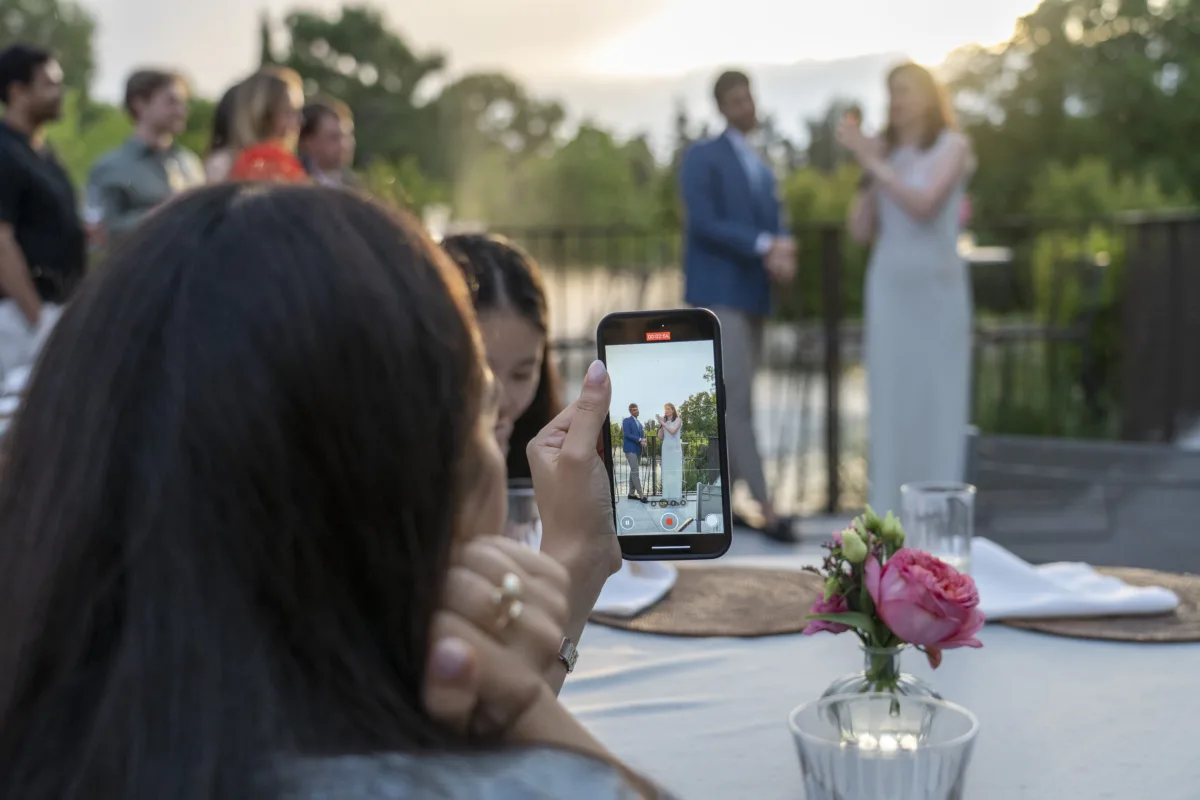 Wedding guest records couple's outdoor ceremony speech on smartphone at a Central Florida wedding venue, capturing the bride and groom at golden hour during an intimate reception dinner