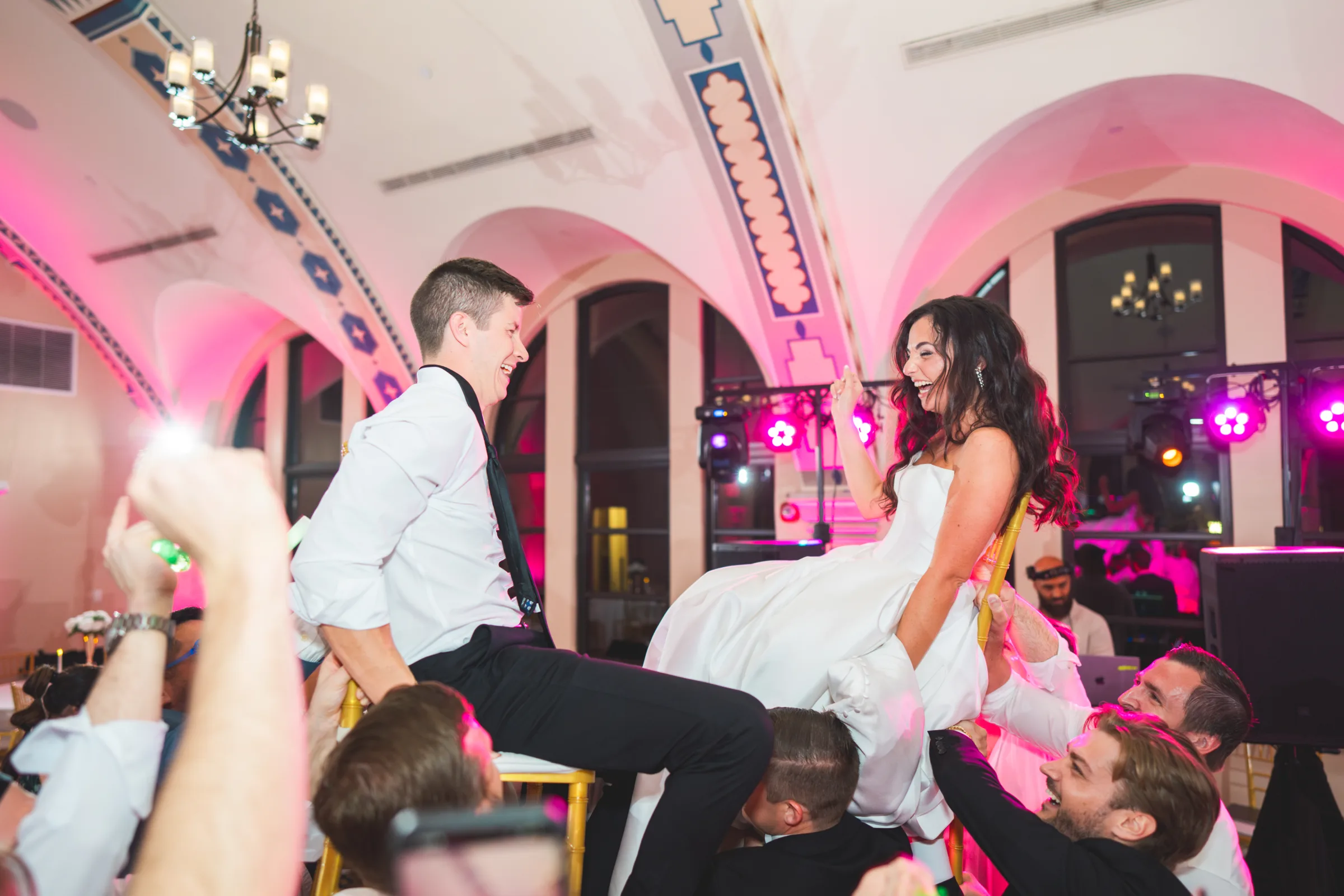 CodyKarinaWedding03 15 2026 1609 - European Inspired Wedding | Rollins College Bride and groom being lifted up on chairs on their packed dance floor with pink lighting at european inspired wedding reception at Rollins College