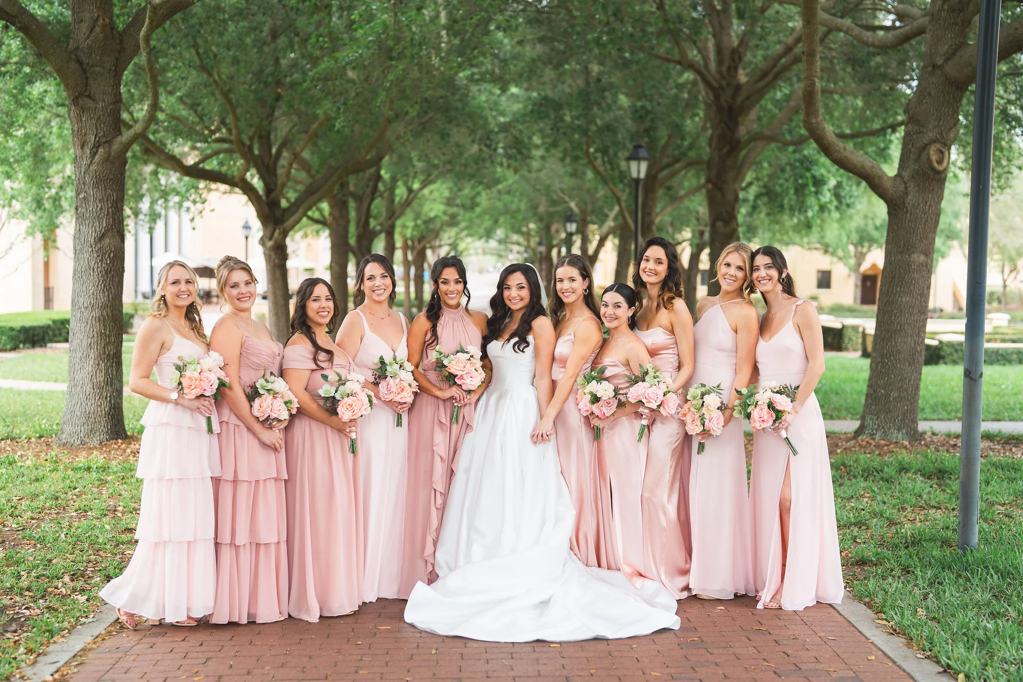 CodyKarinaWedding03.15.2026 113 - European Inspired Wedding | Rollins College Bridesmaids in dusty rose and blush gowns with bride under oak trees at Rollins College European inspired wedding