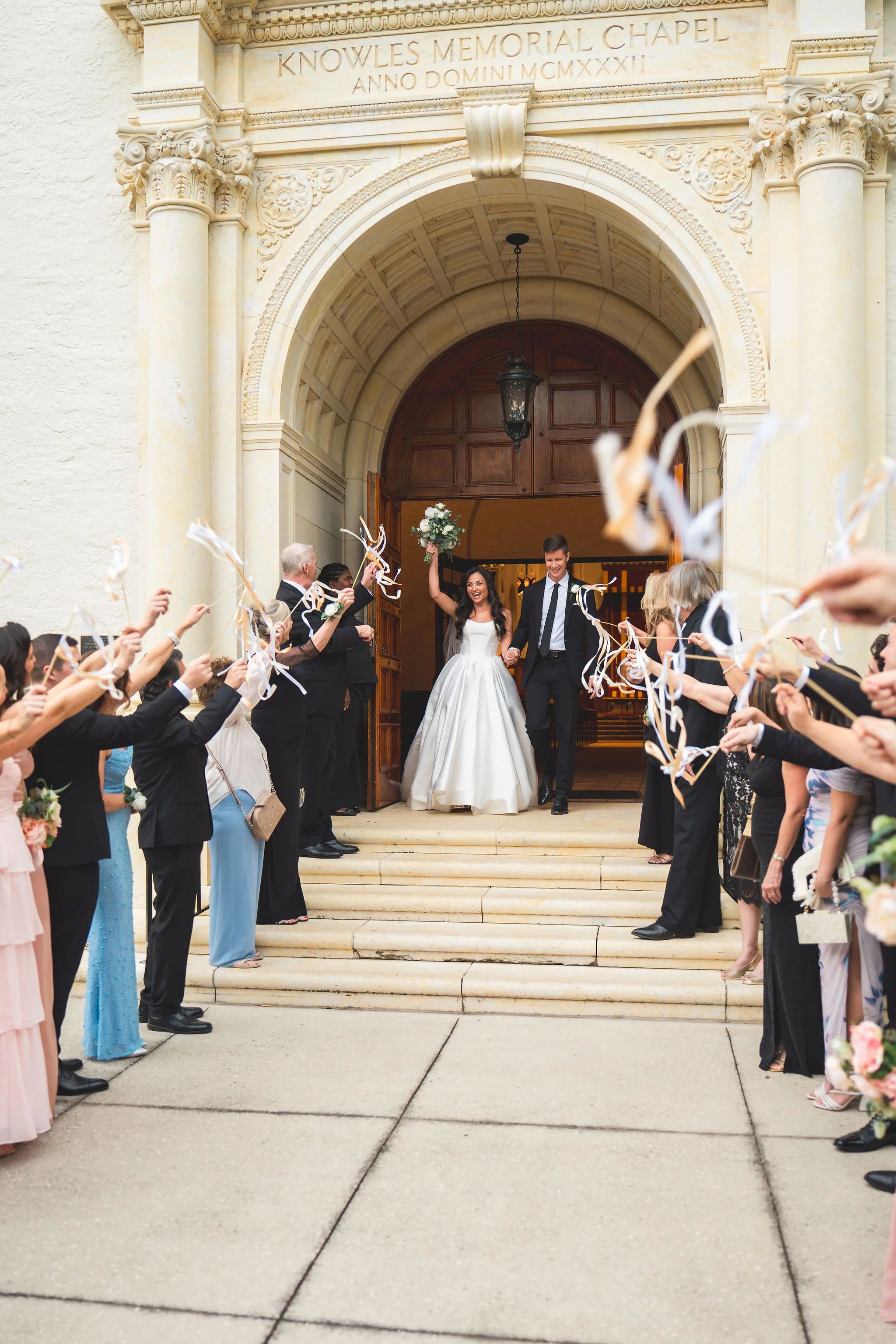CodyKarinaWedding03.15.2026 637 - European Inspired Wedding | Rollins College Couple exits the Chapel after the ceremony, being greeted by their guests waving streamers.
