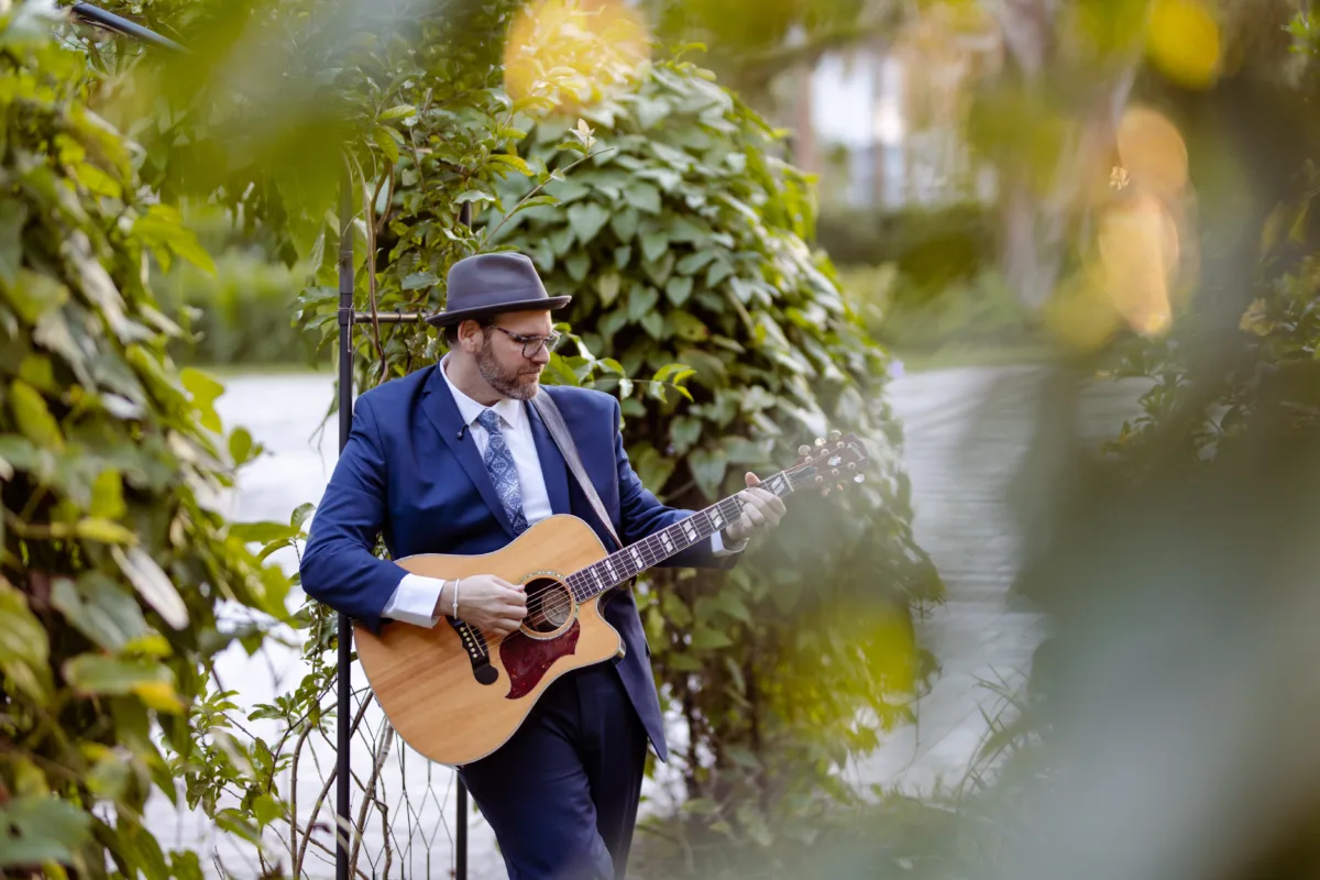 Wedding musician playing acoustic guitar during an outdoor wedding celebration