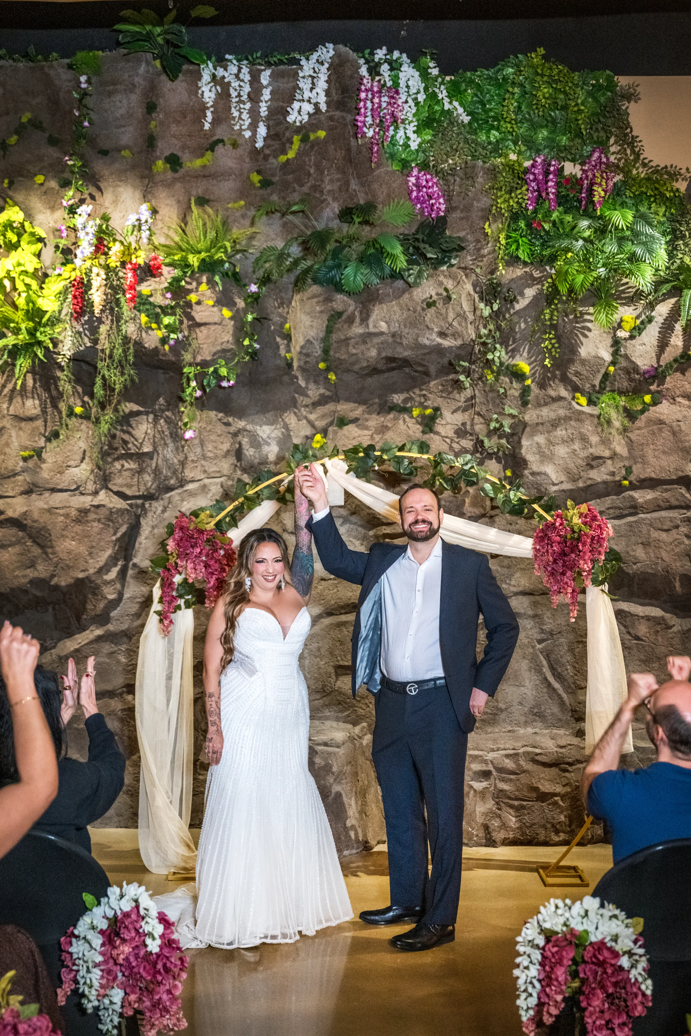 Tropical wedding ceremony with bride and groom beneath a floral arch surrounded by lush greenery