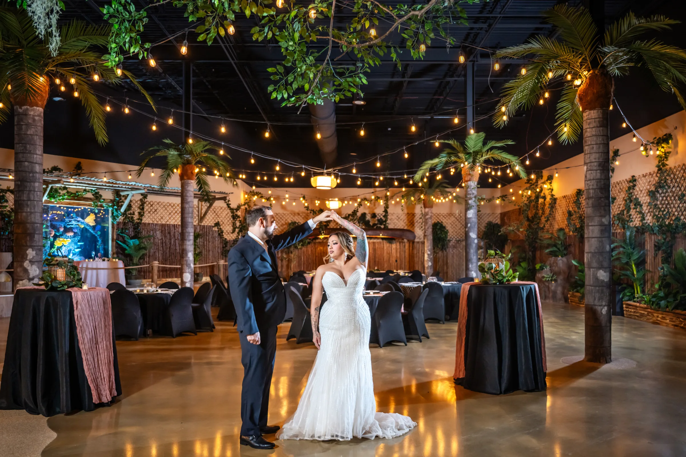 Bride and groom share their first dance under warm string lights surrounded by tropical palm trees and lush greenery at Daytona Aquarium, a unique alternative wedding venue in Daytona Beach Florida