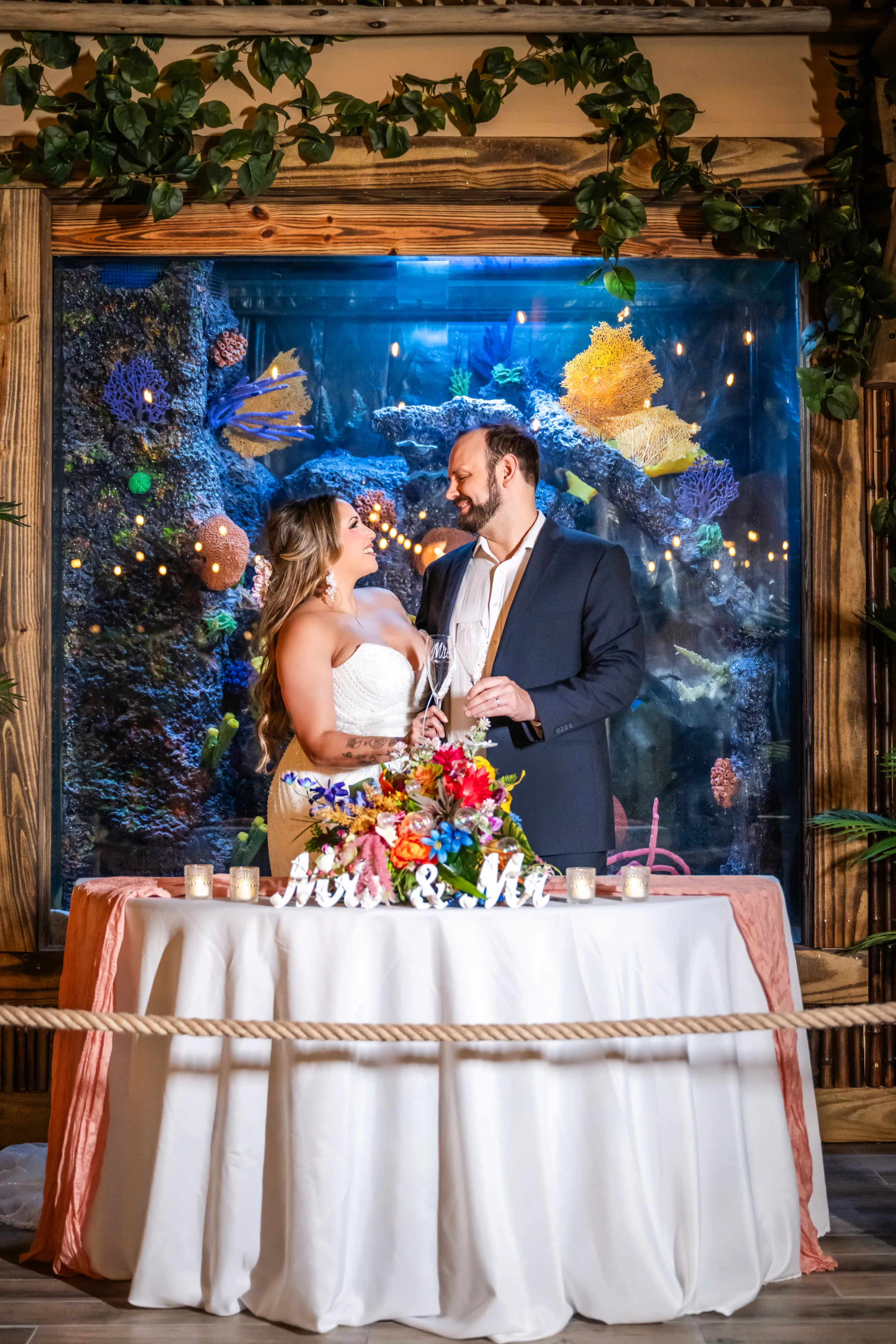 Bride and groom toasting with champagne in front of a colorful coral aquarium sweetheart table