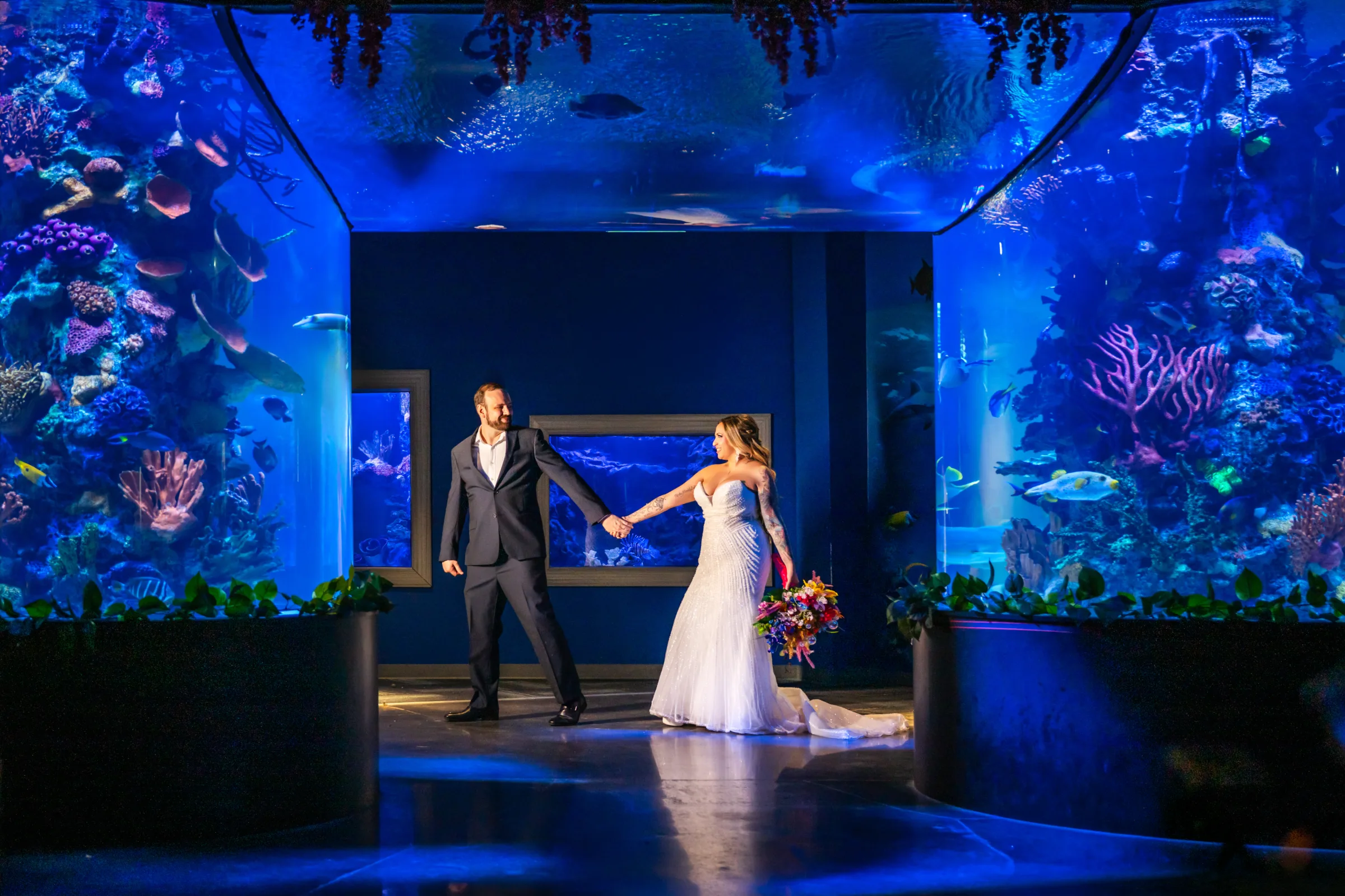 Bride and groom holding hands surrounded by glowing coral reef aquarium tanks at Daytona Aquarium in Daytona Beach Florida during a styled shoot wedding inspiration session