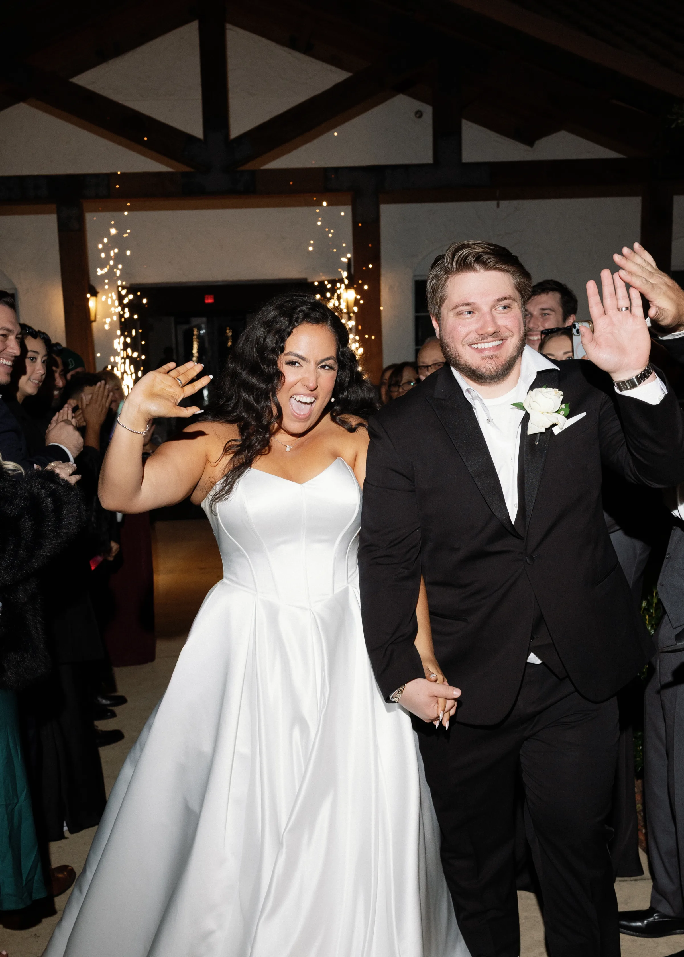 Bride in strapless white gown and groom in black tuxedo wave and celebrate during their grand entrance with cold sparklers at an Orlando Central Florida wedding venue
