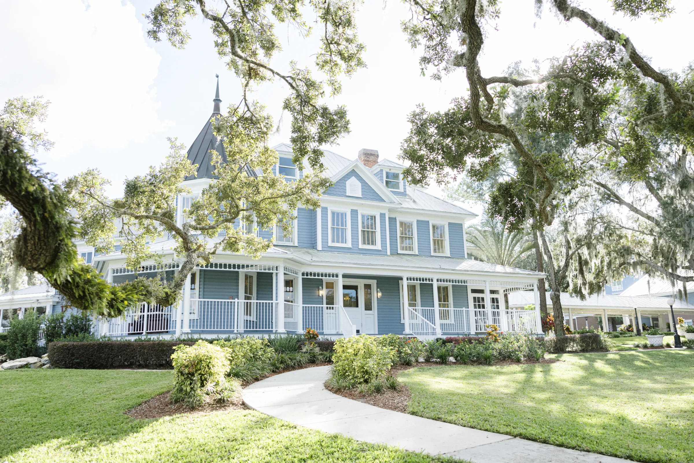 estate central florida wedding venue the highland manor - Wedding Venues Collections Blue Victorian-style wedding venue with wrap-around porch, decorative white railings, and lush oak trees draped with Spanish moss at The Highland Manor wedding venue in Central Florida