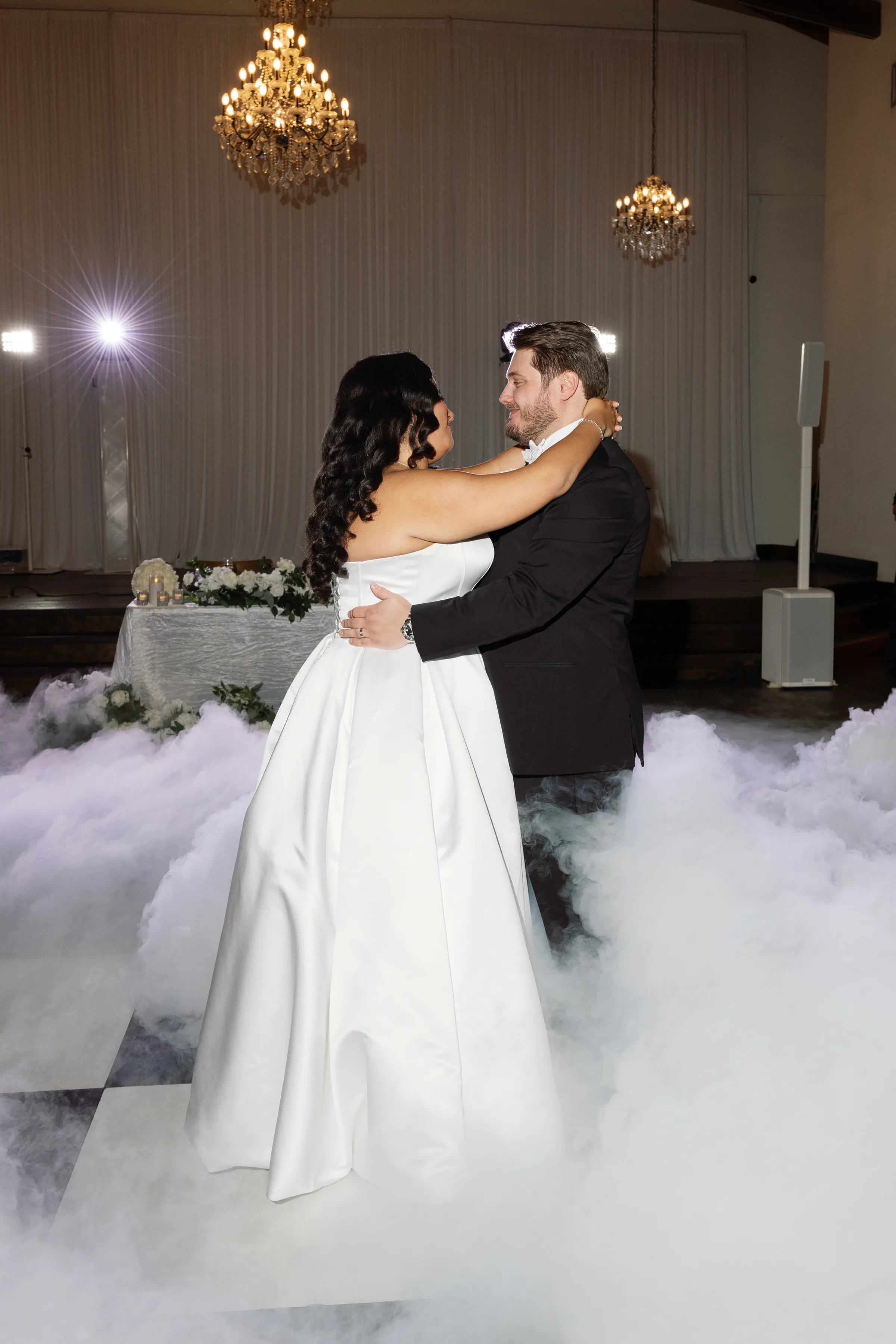 Bride and groom share their first dance on a cloud-covered dance floor created with a dry ice effect at an elegant Orlando wedding venue with crystal chandeliers