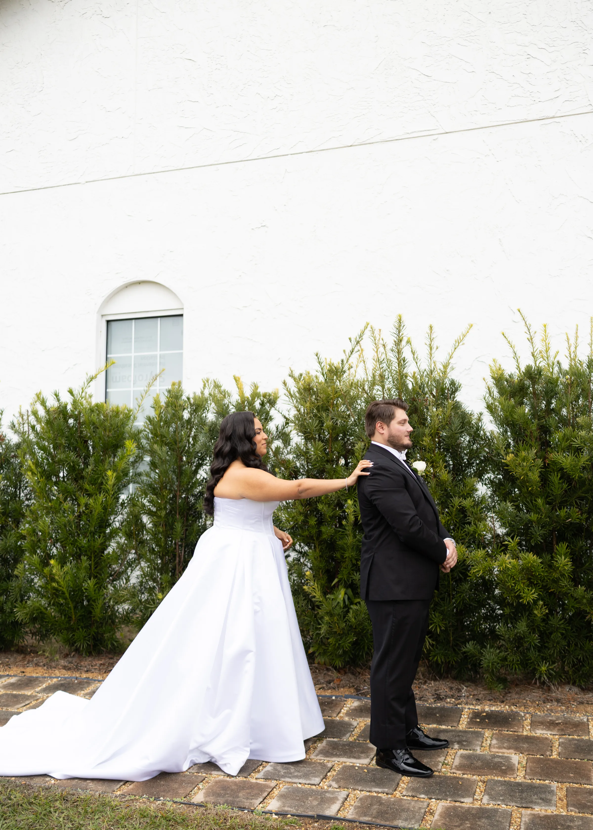 Bride in a white ball gown tapping her groom on the shoulder during a first look moment outside a white stucco wedding venue in Central Florida