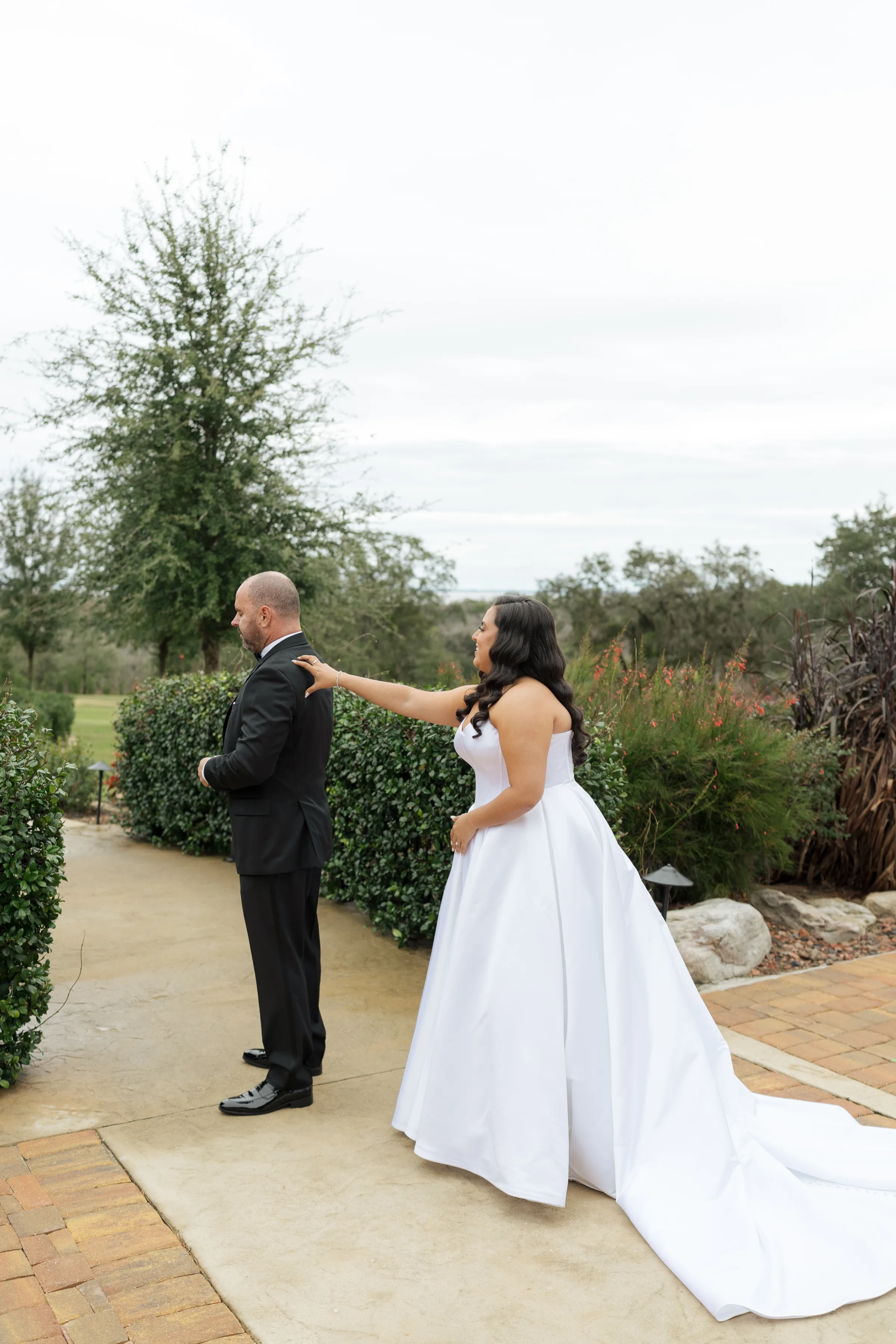 Bride in a strapless white ballgown touches groom's shoulder during an outdoor first look moment at a Central Florida wedding venue surrounded by lush garden greenery