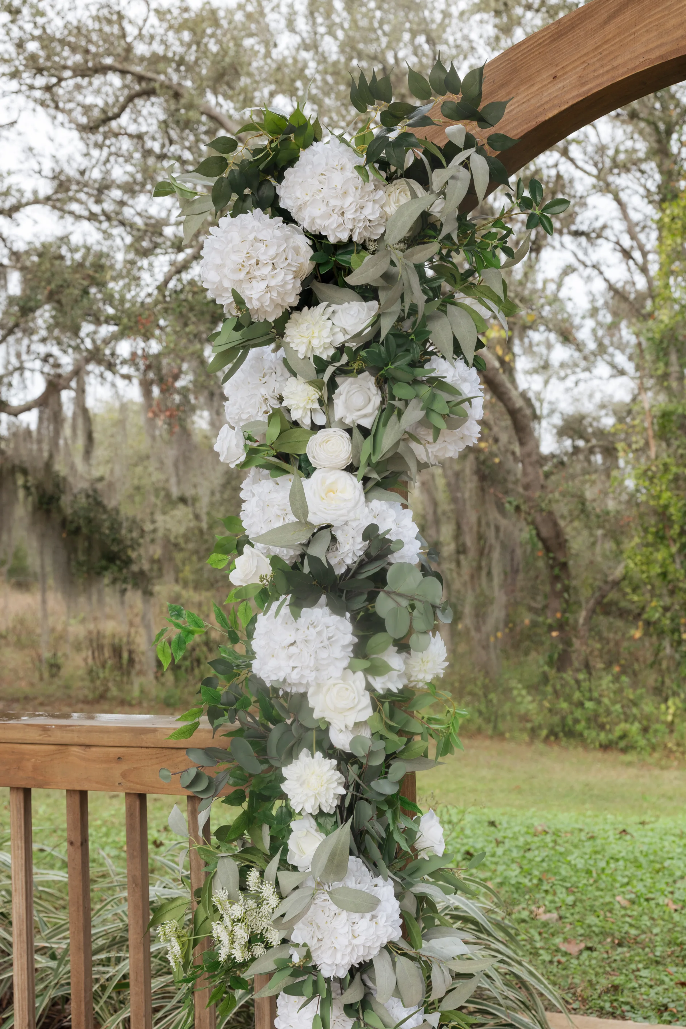 Lush white hydrangea and rose garland draped on a wooden wedding ceremony arch surrounded by eucalyptus greenery at an outdoor Central Florida wedding venue