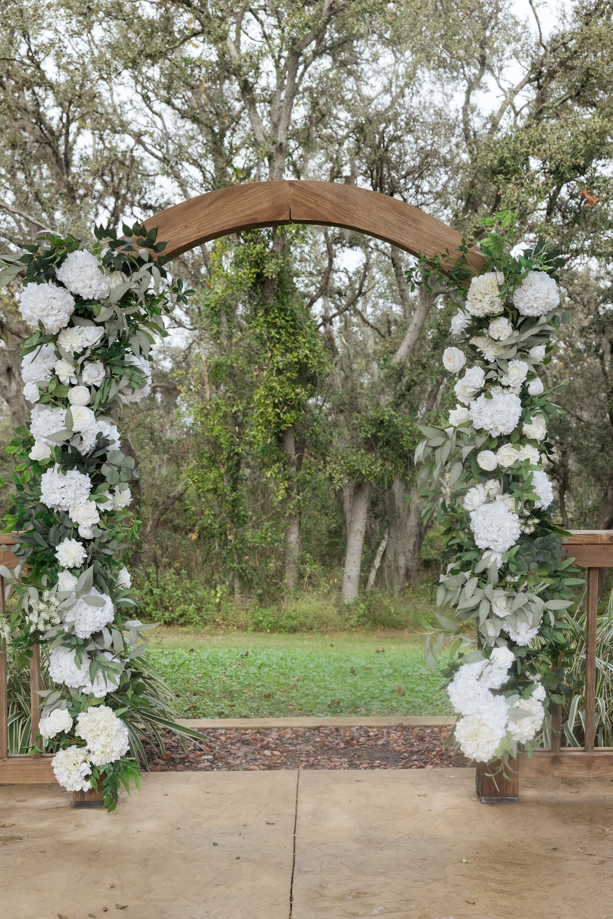 Wooden wedding ceremony arch adorned with white hydrangeas, roses, and lush greenery garlands at an outdoor Central Florida wedding venue