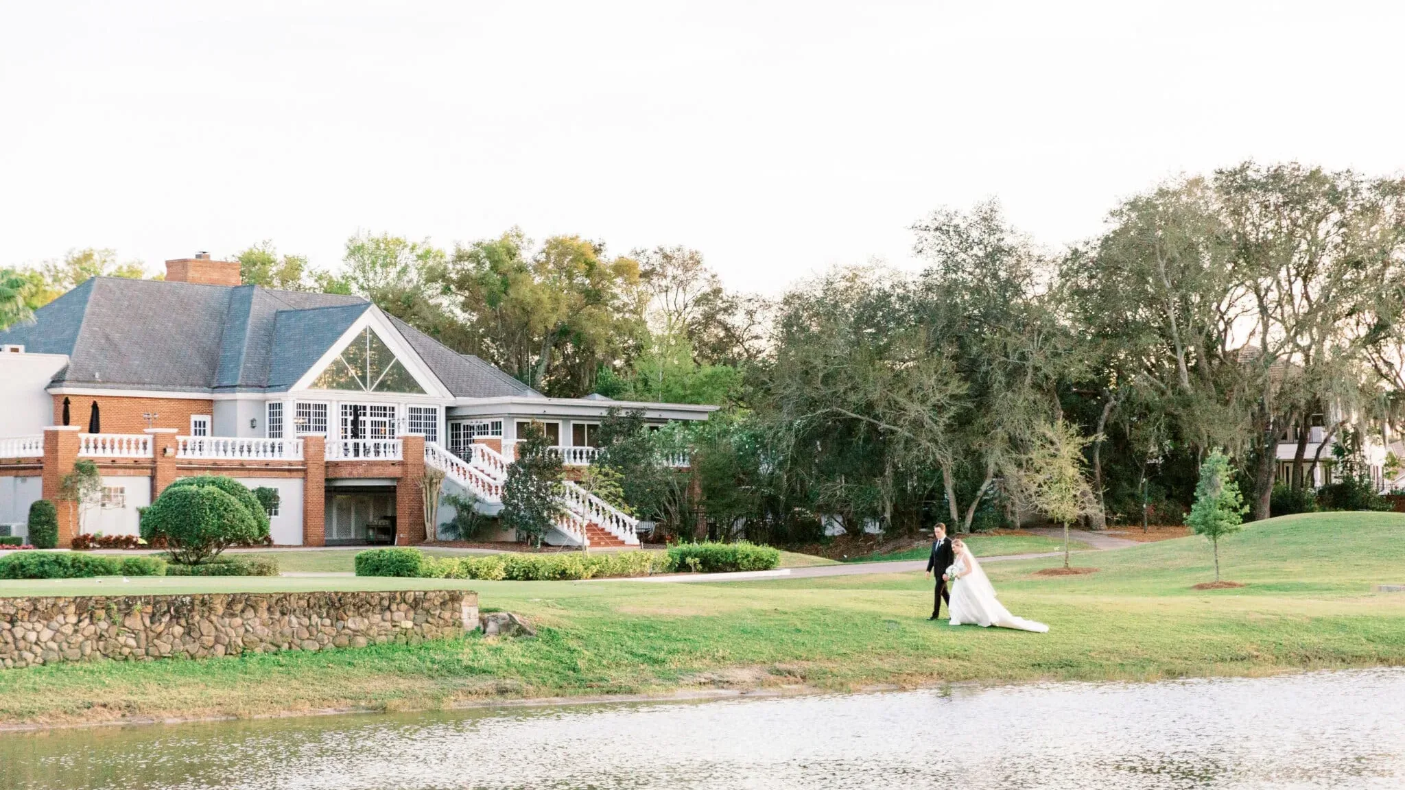 golf country club central florida wedding venue heathrow country club edited - Wedding Venues Collections bride and groom walking along a lakeside lawn at an elegant brick estate wedding venue surrounded by Spanish moss-draped oak trees in Central Florida