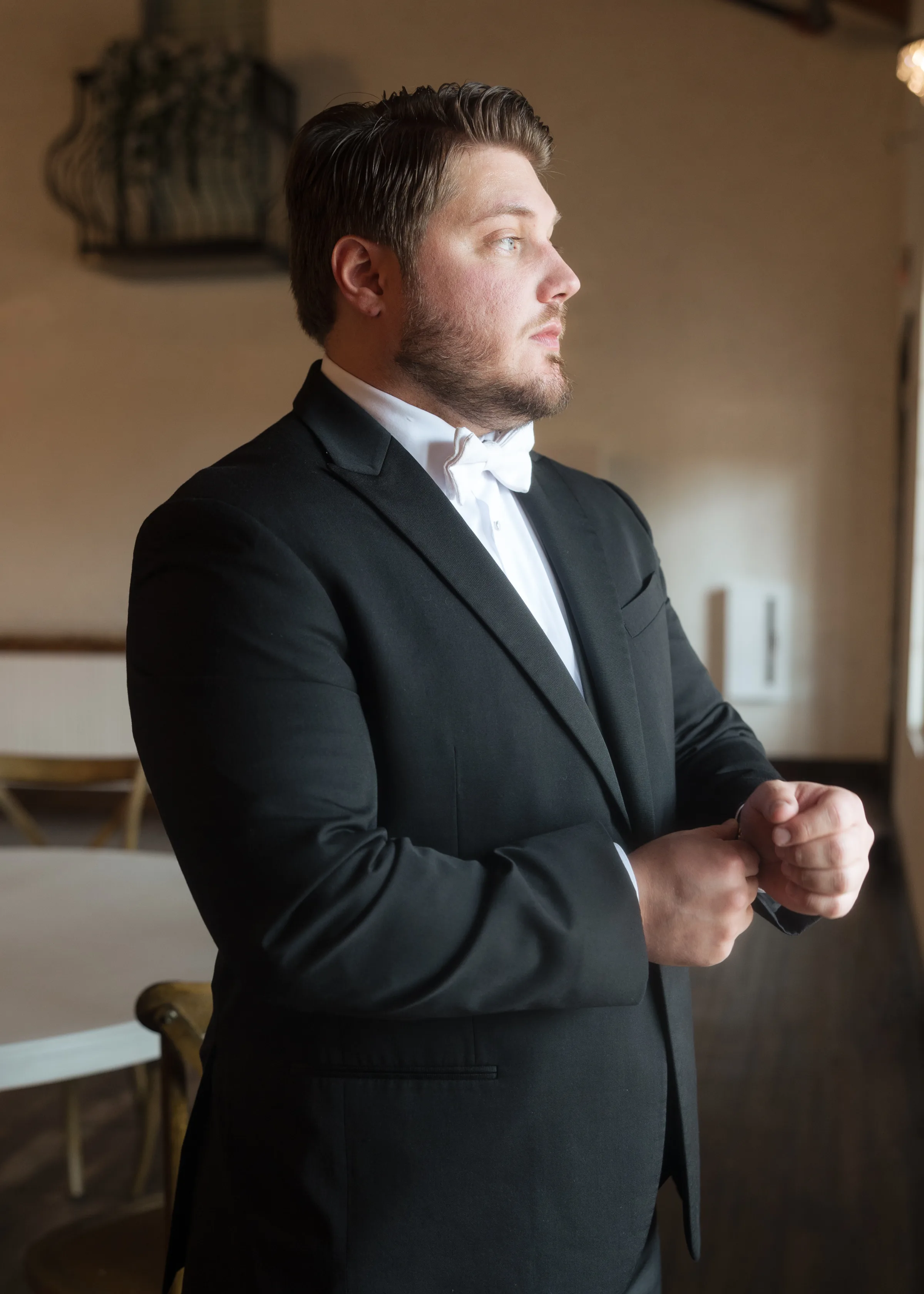 Groom in a black tuxedo and white bow tie adjusting his cufflinks while getting ready for his wedding day in Orlando, Florida