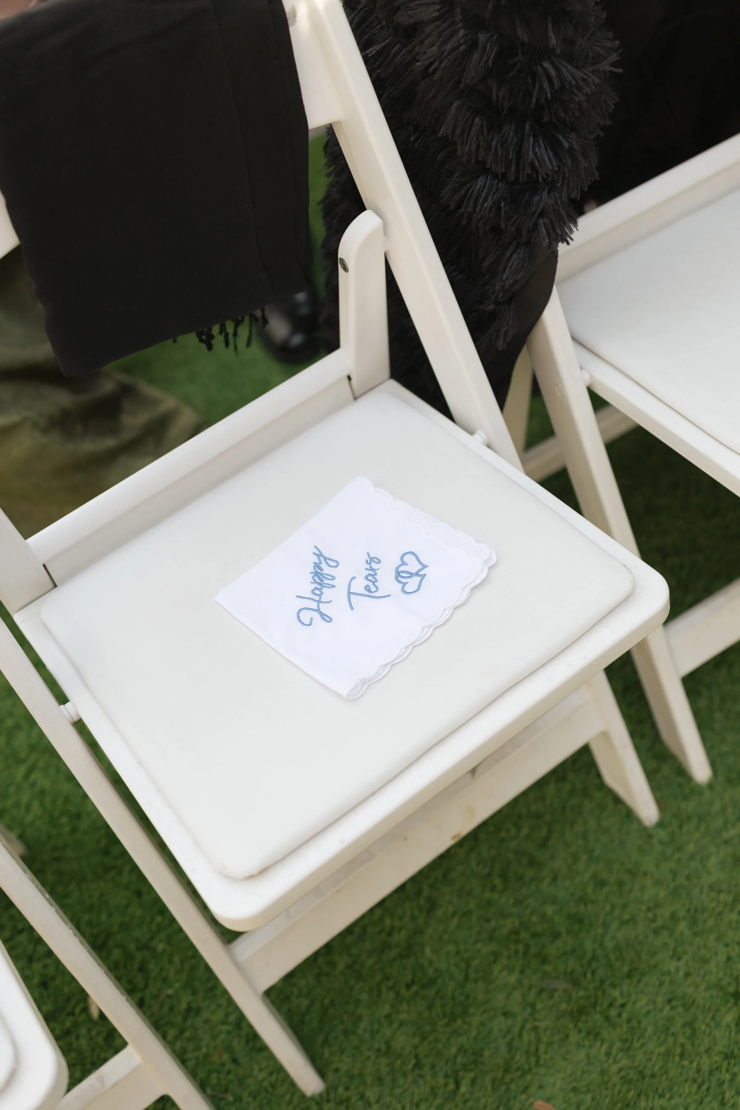 A custom embroidered happy tears handkerchief placed on a white folding chair at an outdoor wedding ceremony in Orlando Florida