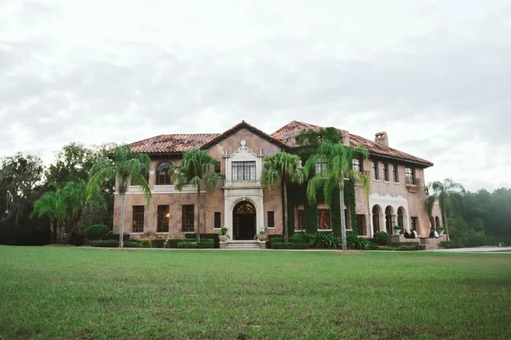 italian inspired central florida wedding venue the howey mansion 1 - Wedding Venues Collections Grand Italian-style wedding venue mansion with terracotta roof, palm trees, arched entryway, and lush green lawn at The Howey Mansion in Central Florida