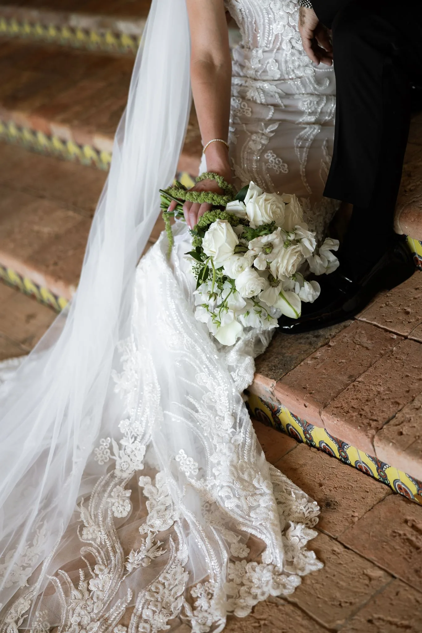 lilac ivory wedding bridal bouquet la hacienda - An Elegant Lilac and Ivory Wedding at La Hacienda on Snow Hill Bride holding a white rose and anemone bouquet with her lace wedding dress train spread across terracotta steps at La Hacienda on Snow Hill in Orlando, Florida