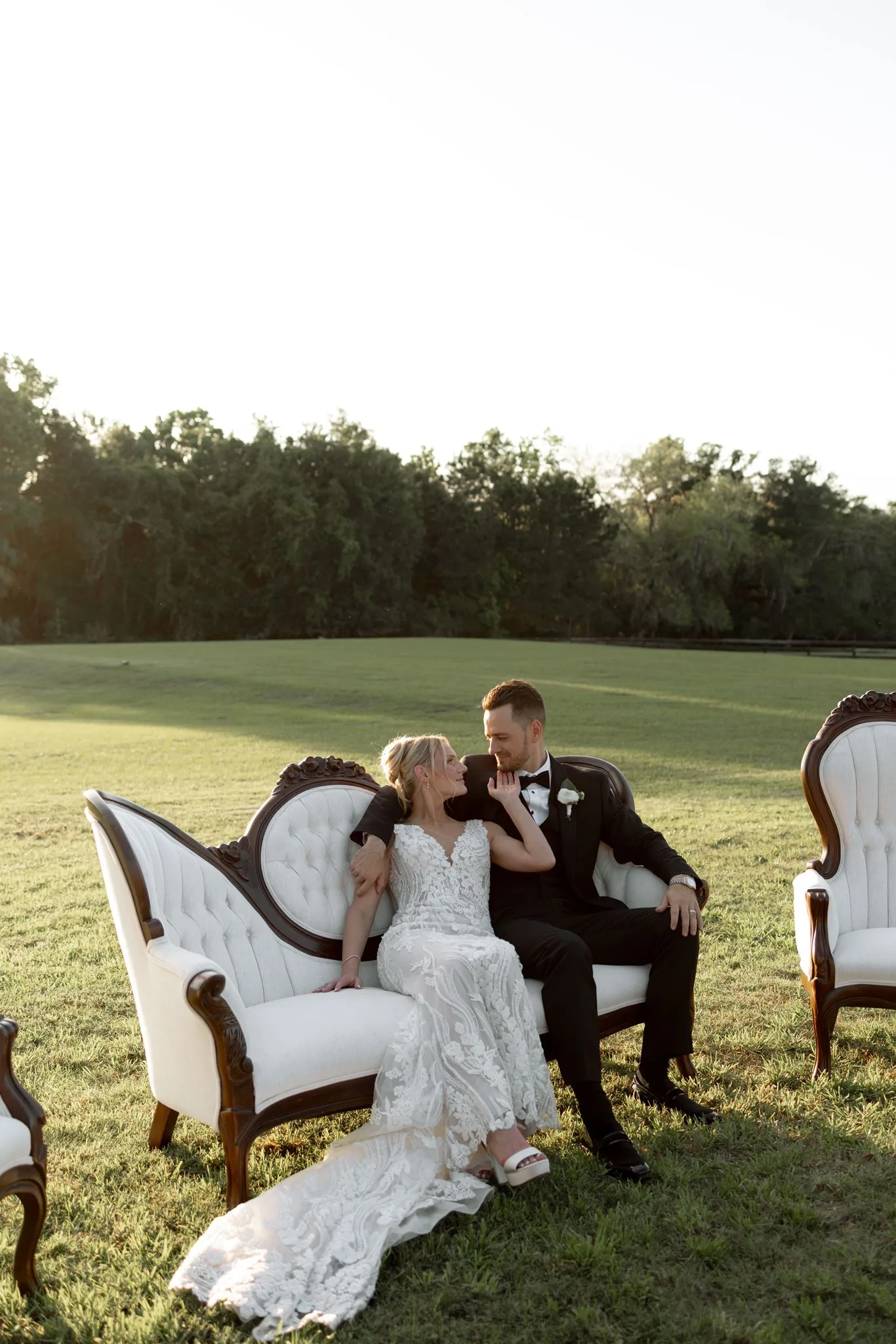 lilac ivory wedding bride groom portrait la hacienda 1 - An Elegant Lilac and Ivory Wedding at La Hacienda on Snow Hill Bride and groom share an intimate moment seated on an ornate white Victorian settee in an open field at La Hacienda on Snow Hill in Central Florida, bride wearing a lace gown with a flowing train for their lilac and ivory spring wedding