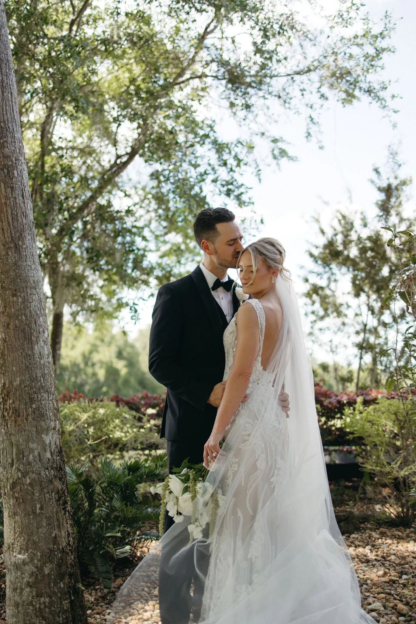 lilac ivory wedding bride groom portrait la hacienda 2 - An Elegant Lilac and Ivory Wedding at La Hacienda on Snow Hill Bride and groom share a romantic moment among lush garden greenery at La Hacienda on Snow Hill in Central Florida, the bride wearing an elegant lace gown with cathedral veil and holding a white cascading bouquet for a lilac and ivory spring wedding