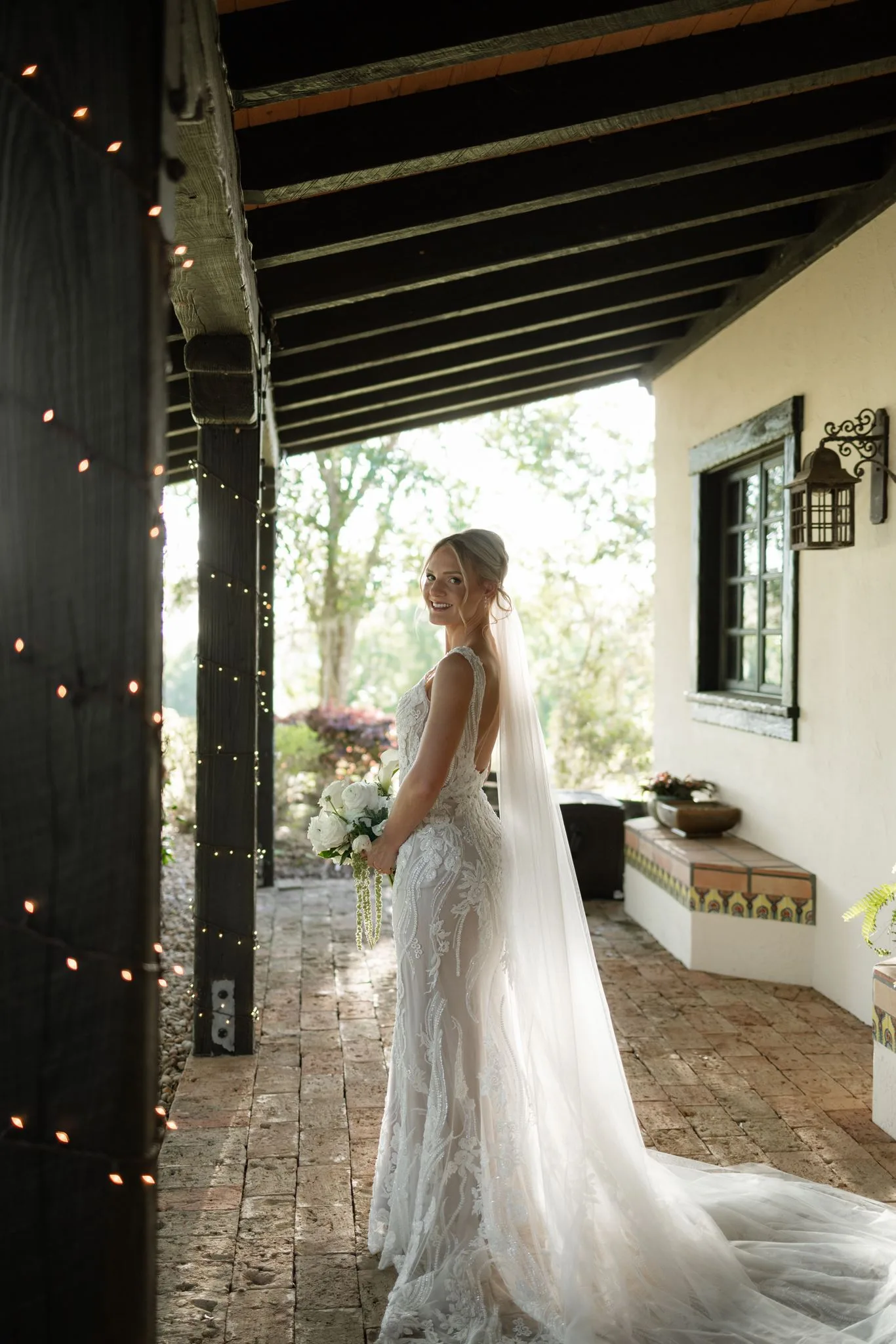 lilac ivory wedding bride la hacienda snow hill 1 - An Elegant Lilac and Ivory Wedding at La Hacienda on Snow Hill Smiling bride in lace gown with cathedral veil holding white bouquet on brick patio at La Hacienda on Snow Hill in Central Florida for a lilac and ivory spring wedding
