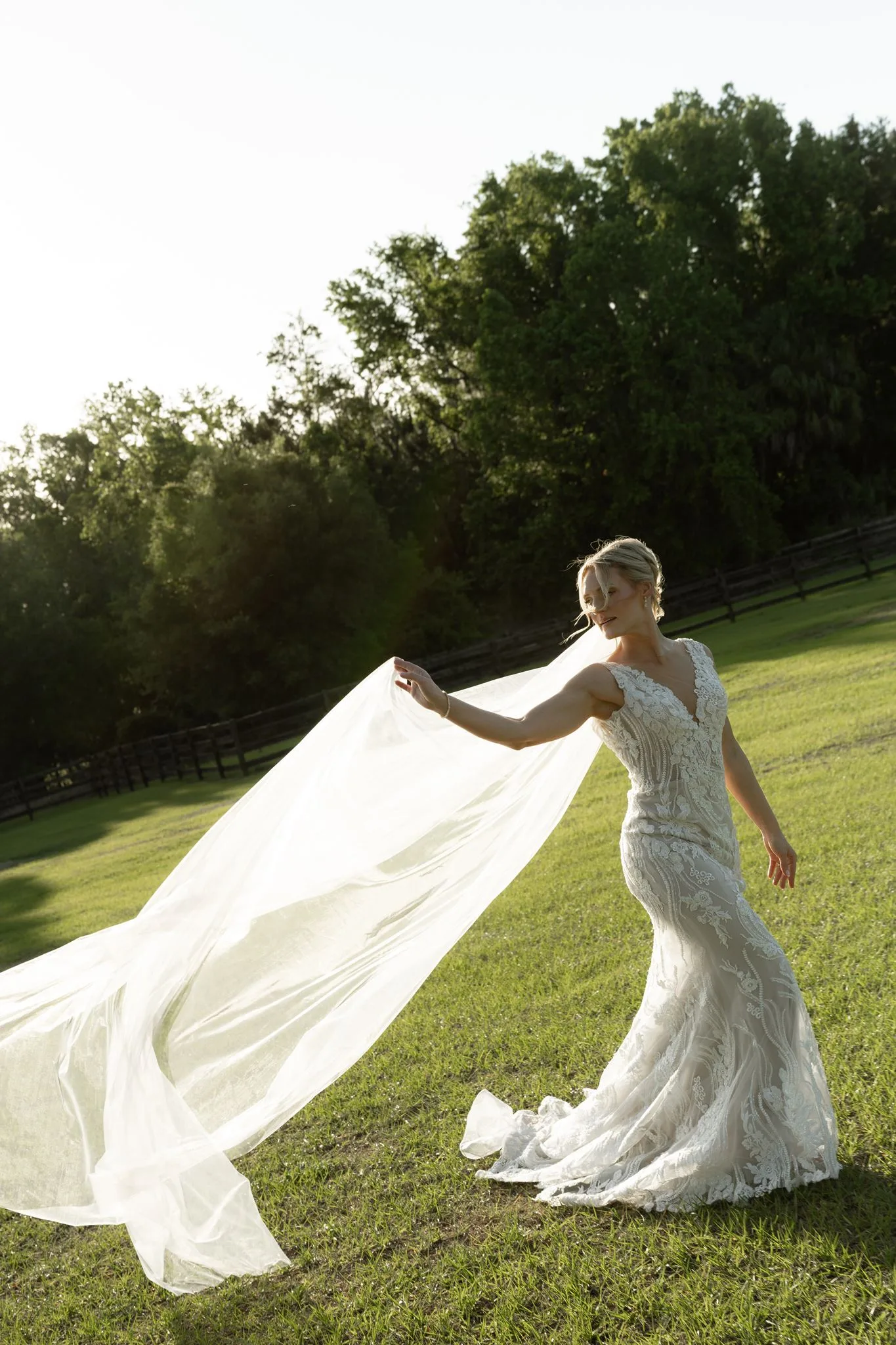 lilac ivory wedding bride veil la hacienda snow hill - An Elegant Lilac and Ivory Wedding at La Hacienda on Snow Hill Bride in fitted lace gown tossing her flowing veil in a sunlit green field at La Hacienda on Snow Hill in Central Florida for a lilac and ivory spring wedding
