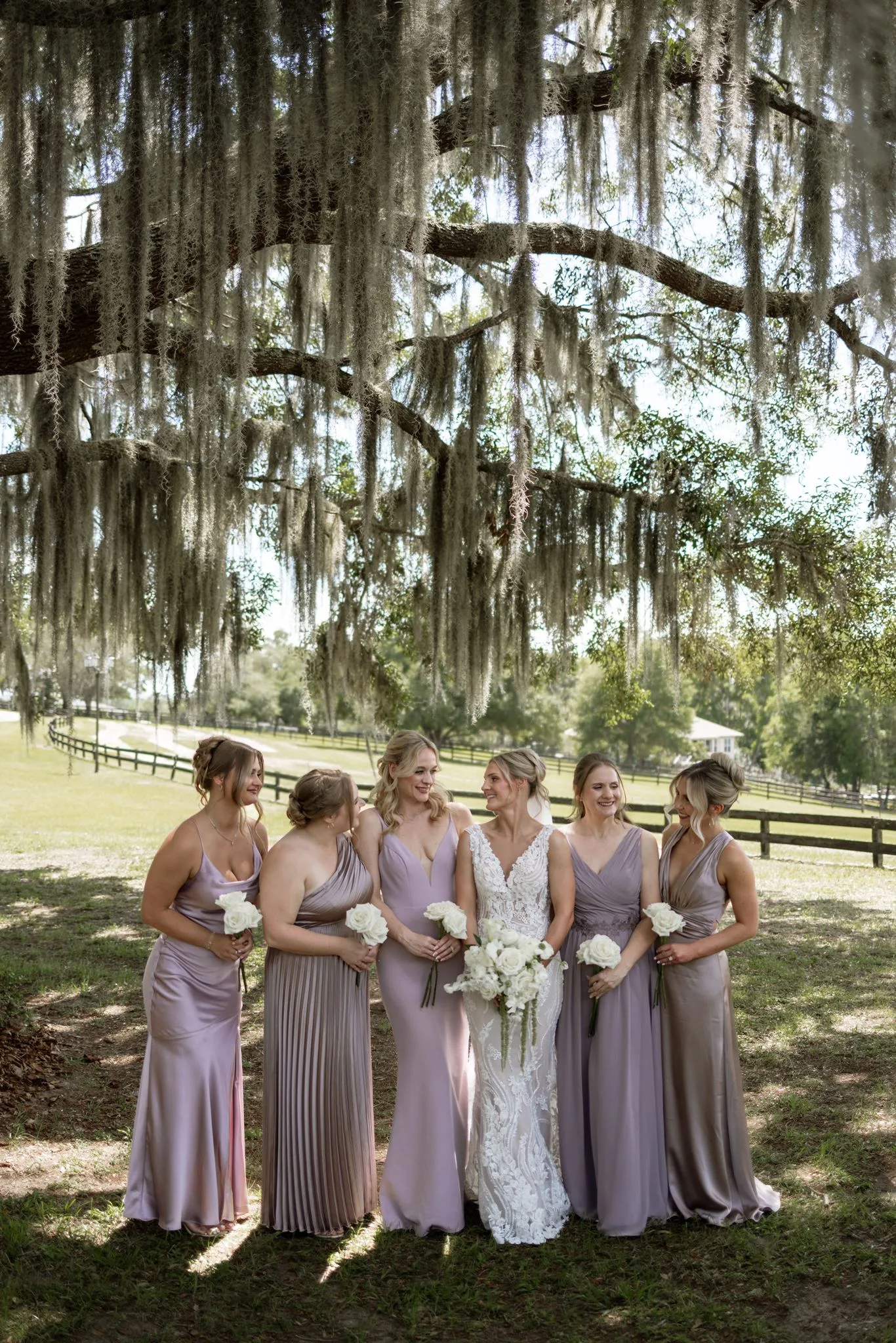 lilac ivory wedding bridesmaids la hacienda snow hill 1 - An Elegant Lilac and Ivory Wedding at La Hacienda on Snow Hill Bride and five bridesmaids in mismatched lilac and mauve gowns holding white floral bouquets under Spanish moss-draped oak trees at La Hacienda on Snow Hill in Central Florida