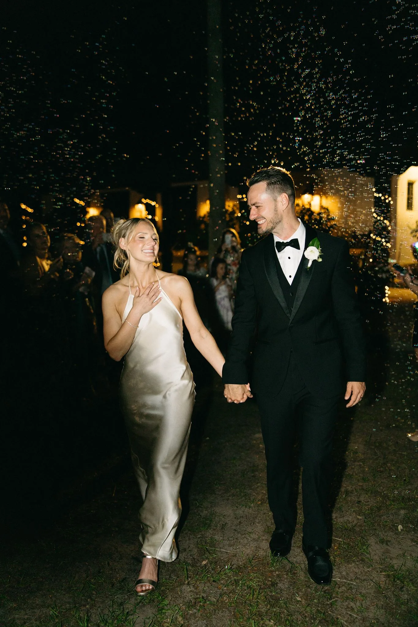 lilac ivory wedding bubble exit la hacienda snow hill - An Elegant Lilac and Ivory Wedding at La Hacienda on Snow Hill Bride in satin slip gown and groom in black tuxedo hold hands during a romantic bubble exit at La Hacienda on Snow Hill in Orlando Florida