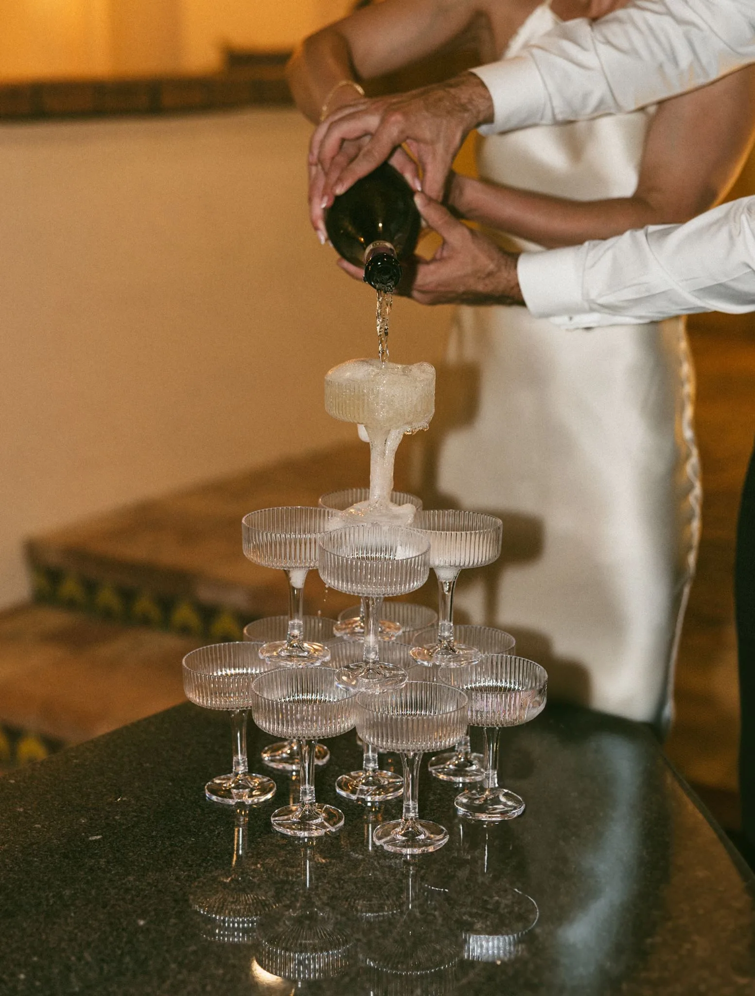 lilac ivory wedding champagne tower la hacienda snow hill 1 - An Elegant Lilac and Ivory Wedding at La Hacienda on Snow Hill Couple pouring champagne tower with ribbed coupe glasses at lilac and ivory wedding reception at La Hacienda on Snow Hill in Central Florida
