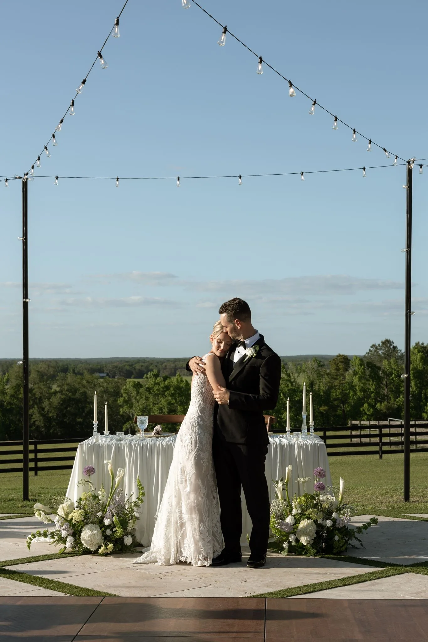 lilac ivory wedding couple la hacienda snow hill - An Elegant Lilac and Ivory Wedding at La Hacienda on Snow Hill Bride and groom share a romantic embrace on an outdoor dance floor surrounded by lilac and ivory floral arrangements and string lights at La Hacienda on Snow Hill in Central Florida