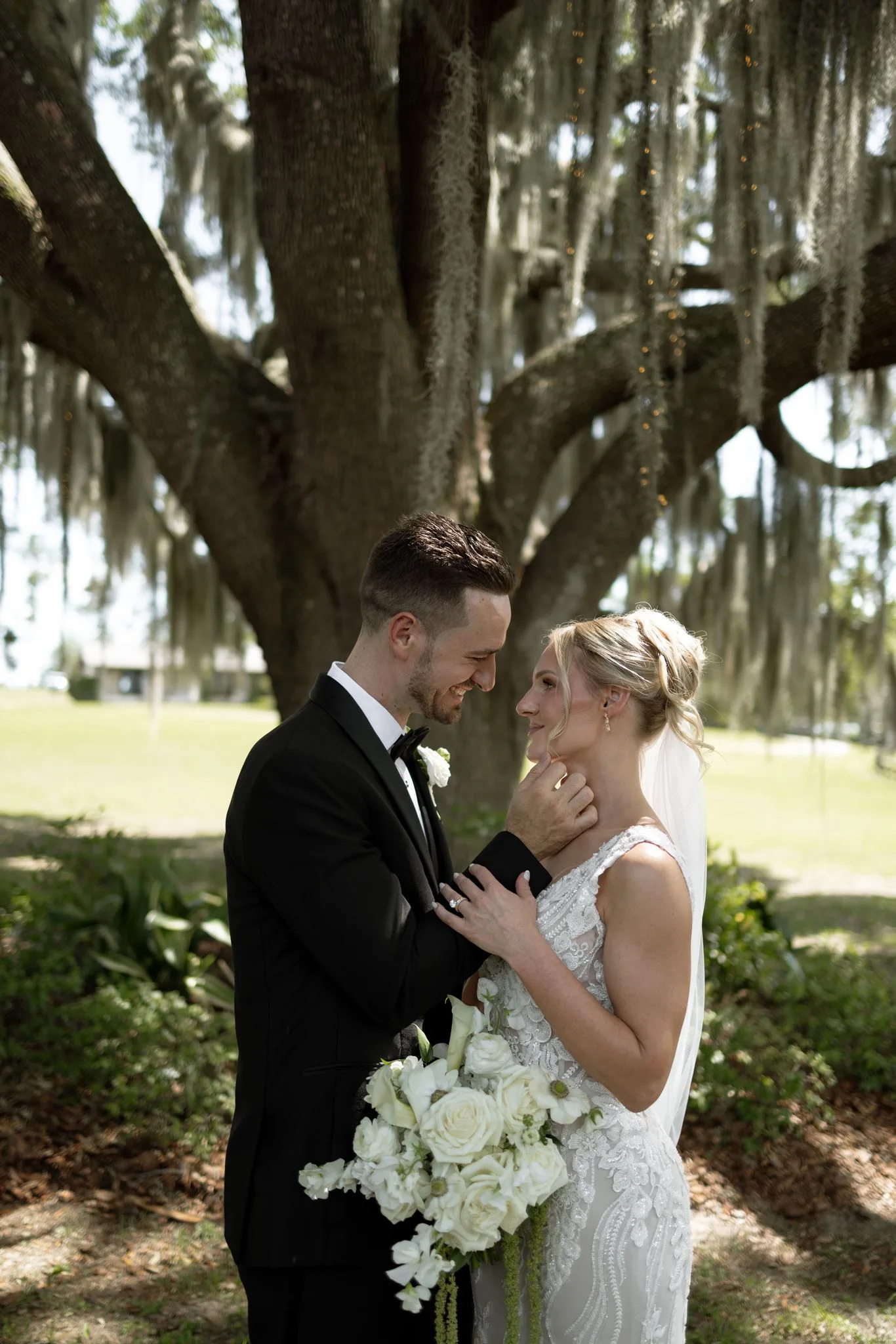 lilac ivory wedding couple portrait la hacienda snow hill - An Elegant Lilac and Ivory Wedding at La Hacienda on Snow Hill Bride and groom share an intimate moment under Spanish moss draped oak trees at La Hacienda on Snow Hill in Orlando, Florida, bride holding a lush white rose bouquet in a lace wedding gown
