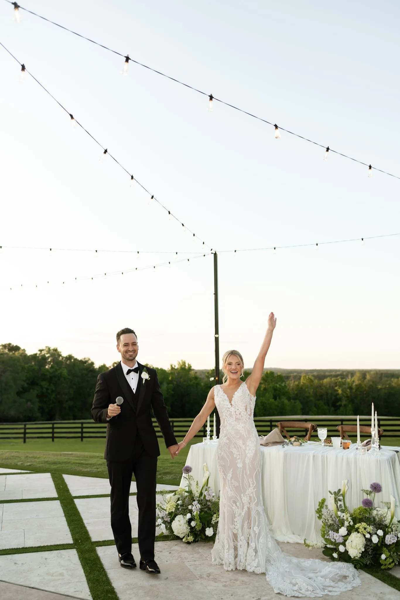 lilac ivory wedding couple toast la hacienda snow hill - An Elegant Lilac and Ivory Wedding at La Hacienda on Snow Hill Bride and groom celebrating with a joyful toast at their lilac and ivory outdoor wedding reception at La Hacienda on Snow Hill in Central Florida, surrounded by lush floral arrangements and string lights