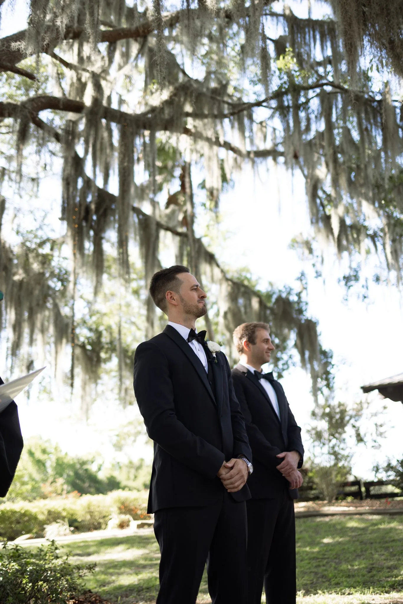lilac ivory wedding groom altar la hacienda snow hill - An Elegant Lilac and Ivory Wedding at La Hacienda on Snow Hill Groom in black tuxedo with white boutonniere watches bride walk down the aisle under Spanish moss-draped oak trees at La Hacienda on Snow Hill in Orlando, Florida