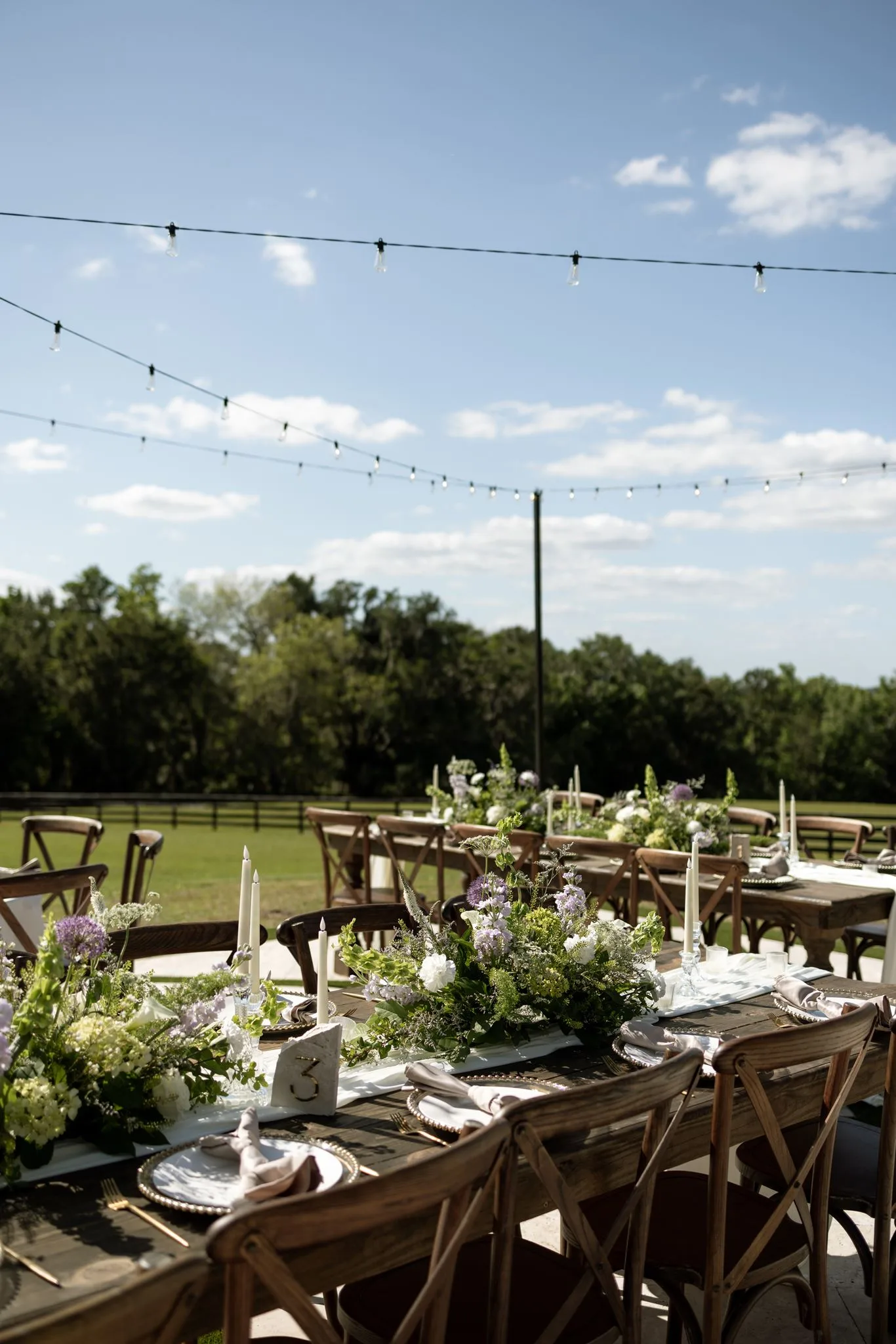 lilac ivory wedding outdoor tablescape la hacienda snow hill - An Elegant Lilac and Ivory Wedding at La Hacienda on Snow Hill Lilac and ivory outdoor wedding reception tablescape with lush greenery centerpieces, taper candles, and string lights at La Hacienda on Snow Hill in Central Florida
