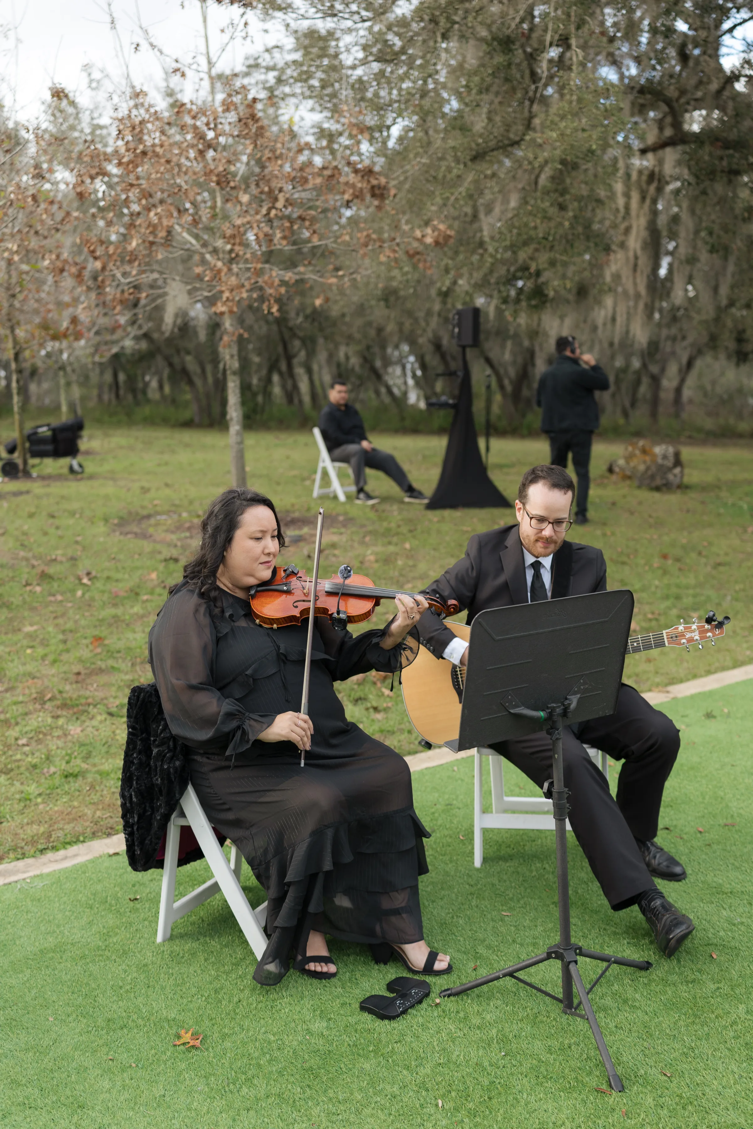 A violinist and acoustic guitarist in formal black attire perform live music at an outdoor wedding ceremony in Orlando, Florida