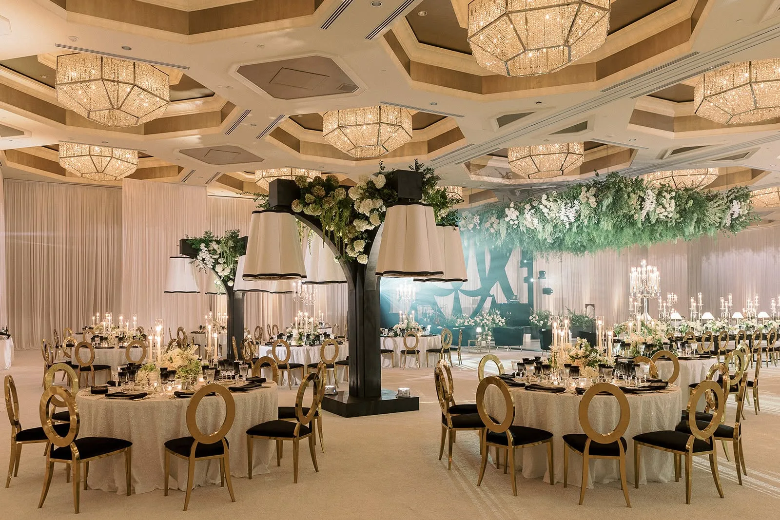 Elegant luxury ballroom wedding reception at the Four Seasons Resort in Central Florida featuring gold oval-back chairs, crystal chandeliers, dramatic floral tree centerpiece with white hydrangeas, and suspended greenery canopy installation