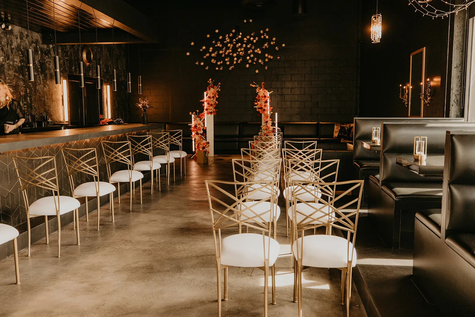 moody central florida wedding venue zymarium meadery 2 - Wedding Venues Collections Gold chiavari chairs arranged in ceremony rows with tall floral pedestals featuring coral and orange blooms creating an aisle at an elegant dark-walled wedding venue at Zymarium Meadery in Orlando Central Florida