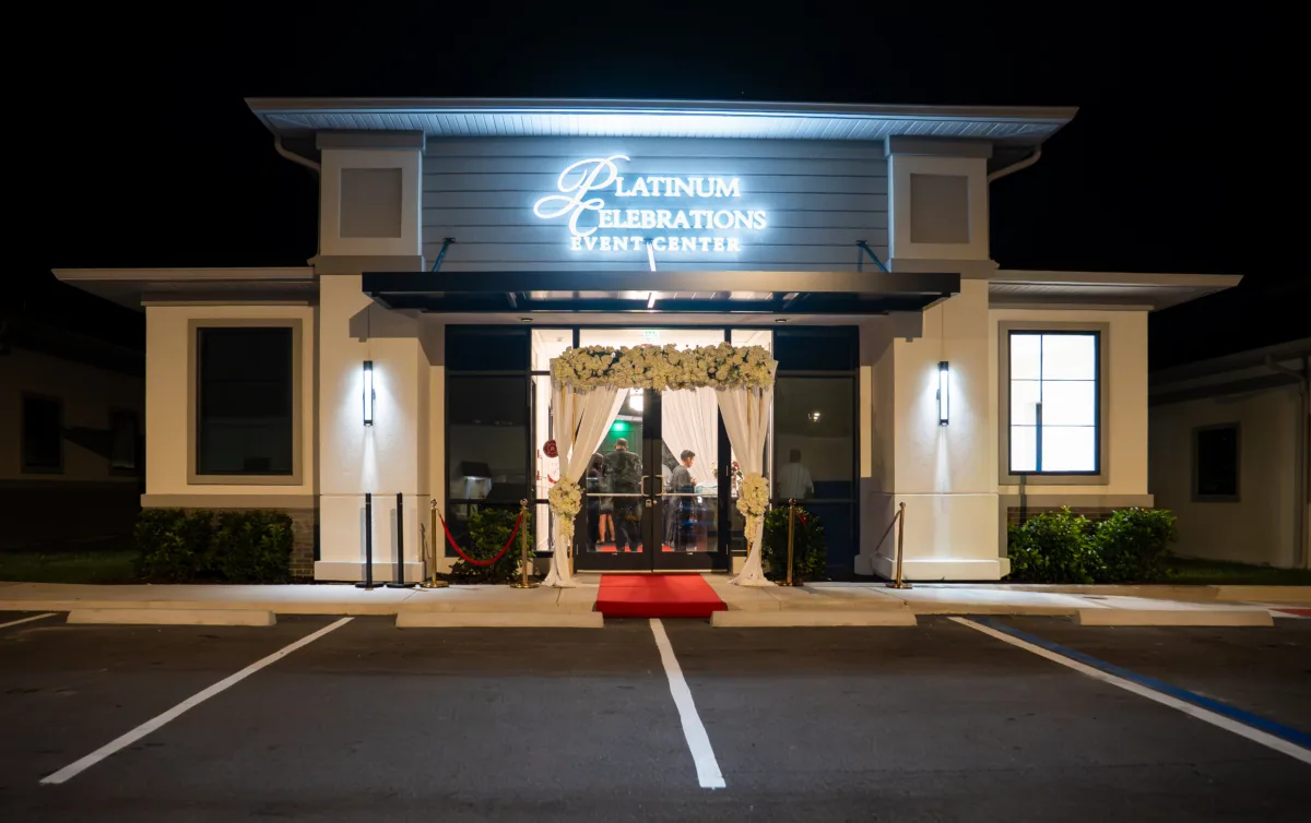 Platinum Celebrations Event Center exterior at night with red carpet entrance, floral arch, and illuminated signage in Apopka, Florida, an affordable ballroom and banquet hall wedding venue in Central Florida