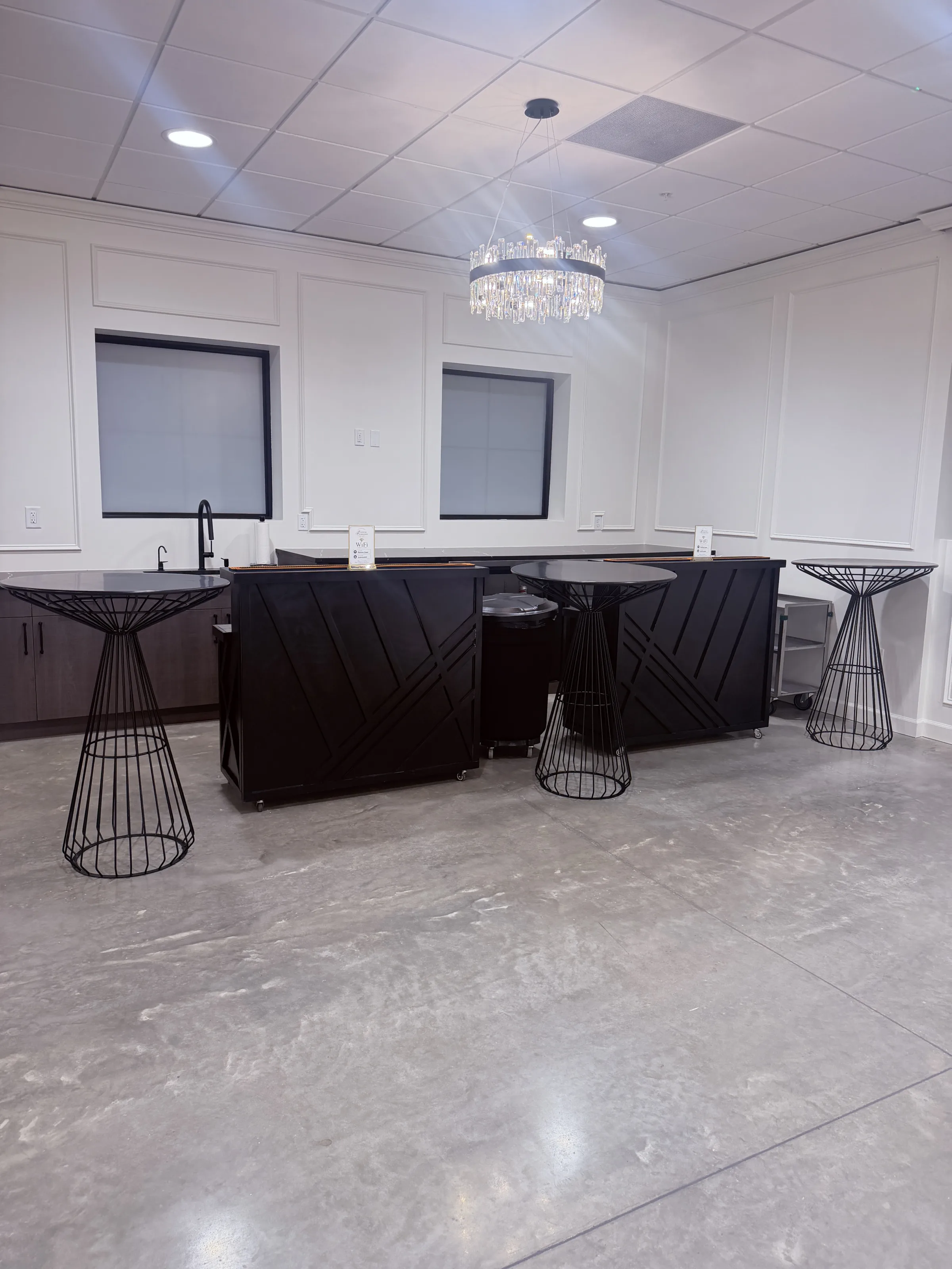 Modern black bar stations with geometric panel design and wire frame high-top cocktail tables beneath a crystal chandelier at Platinum Celebrations Event Center banquet hall in Apopka Florida