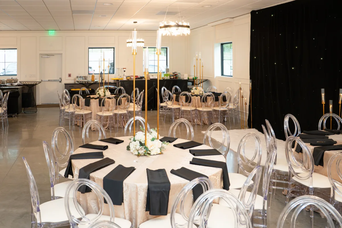 Elegant ballroom reception setup at Platinum Celebrations Event Center in Apopka Florida featuring round tables with champagne sequin linens, black napkins, white floral centerpieces, tall gold candelabras, and acrylic ghost chairs under crystal chandeliers