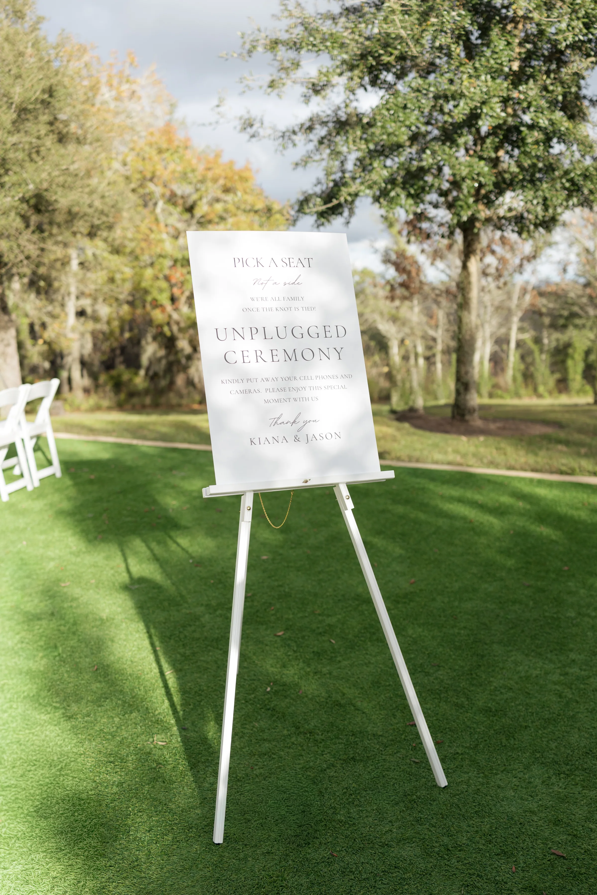 Elegant white unplugged ceremony sign on easel at an outdoor Orlando wedding venue asking guests to put away phones and cameras for Kiana and Jason