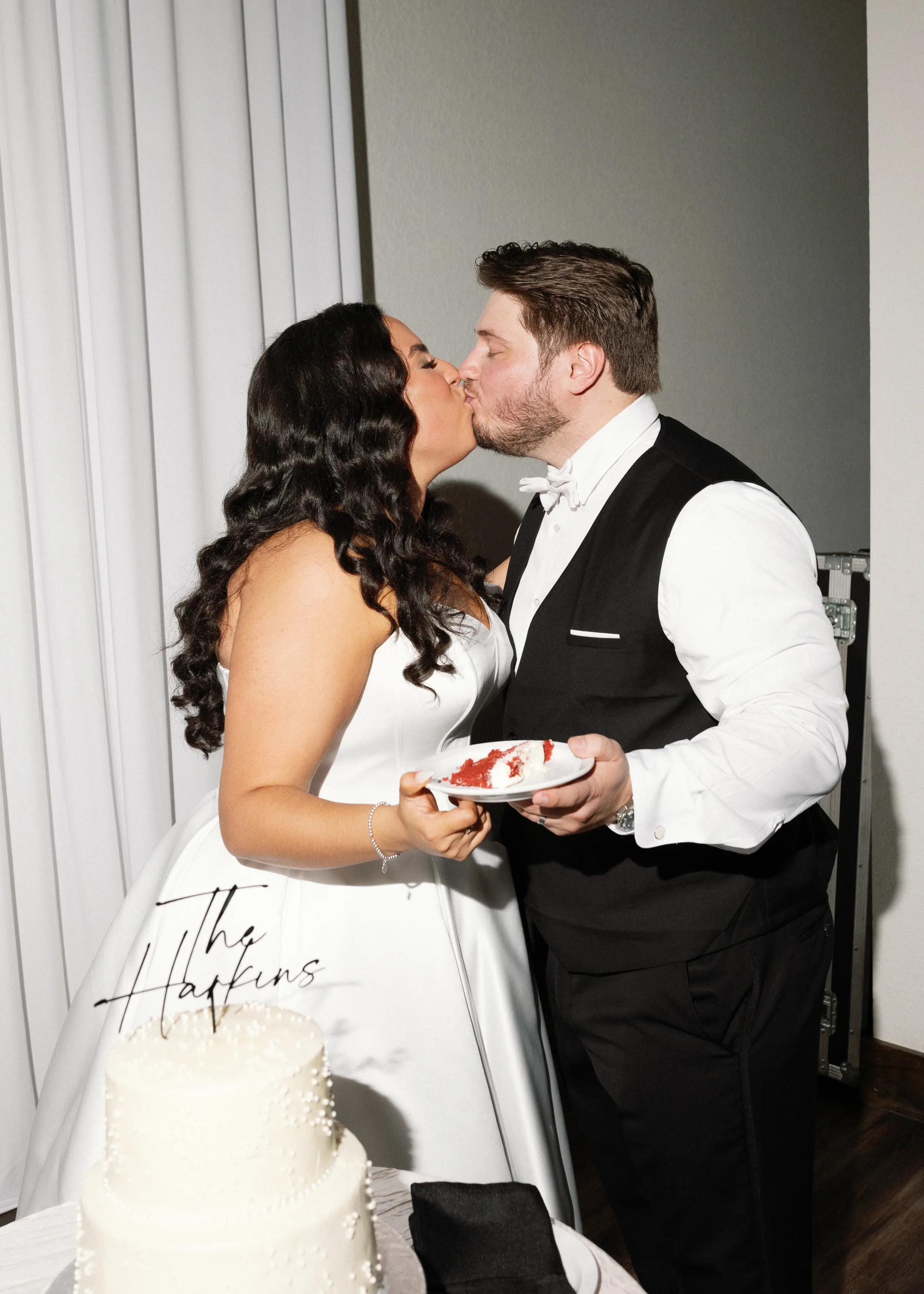 Bride and groom sharing a kiss while holding plates of red velvet wedding cake during their reception, The Harkins wedding in Orlando Florida