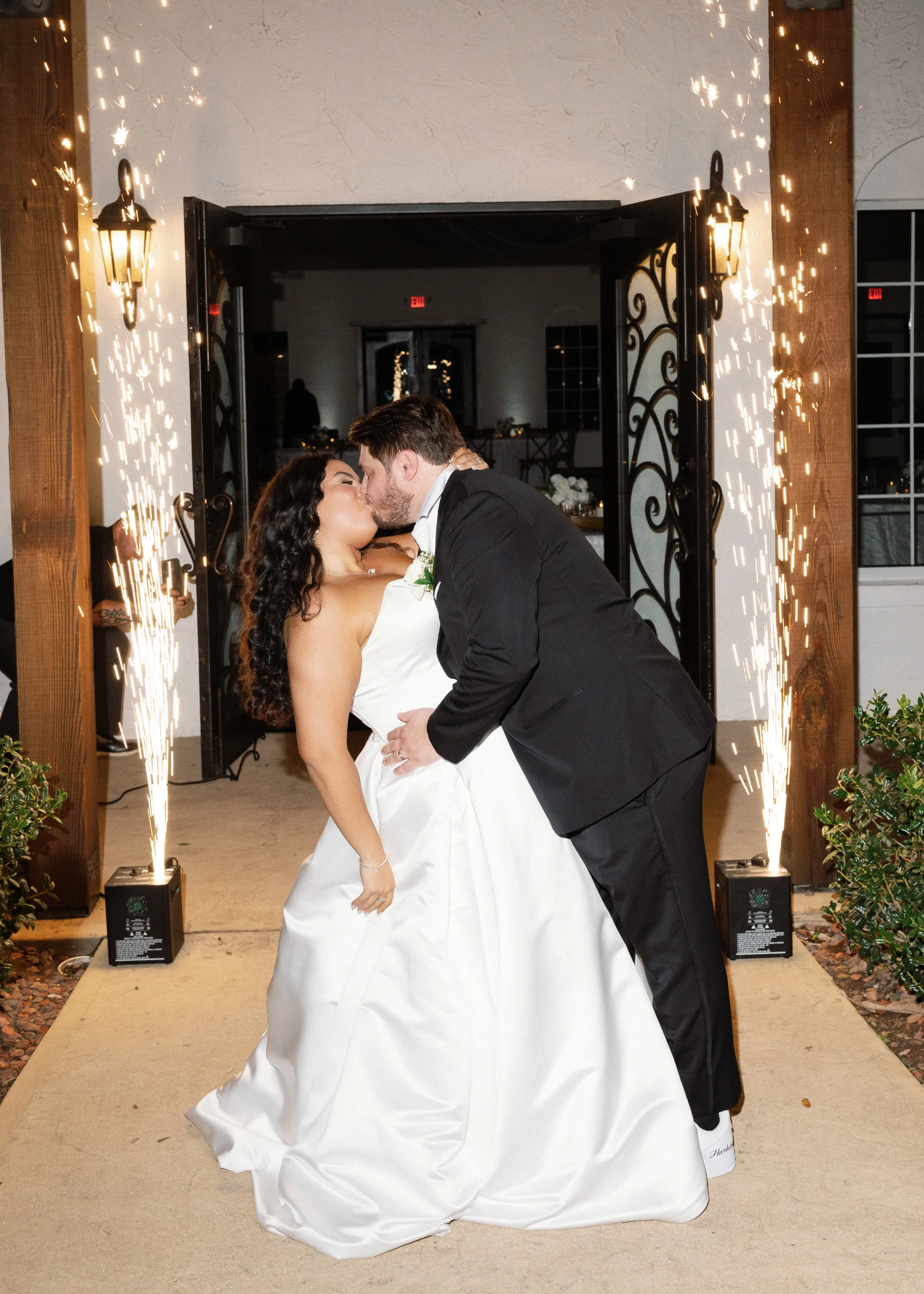 Bride and groom share a romantic dip kiss framed by cold spark fountains during their wedding venue exit in Orlando, Central Florida