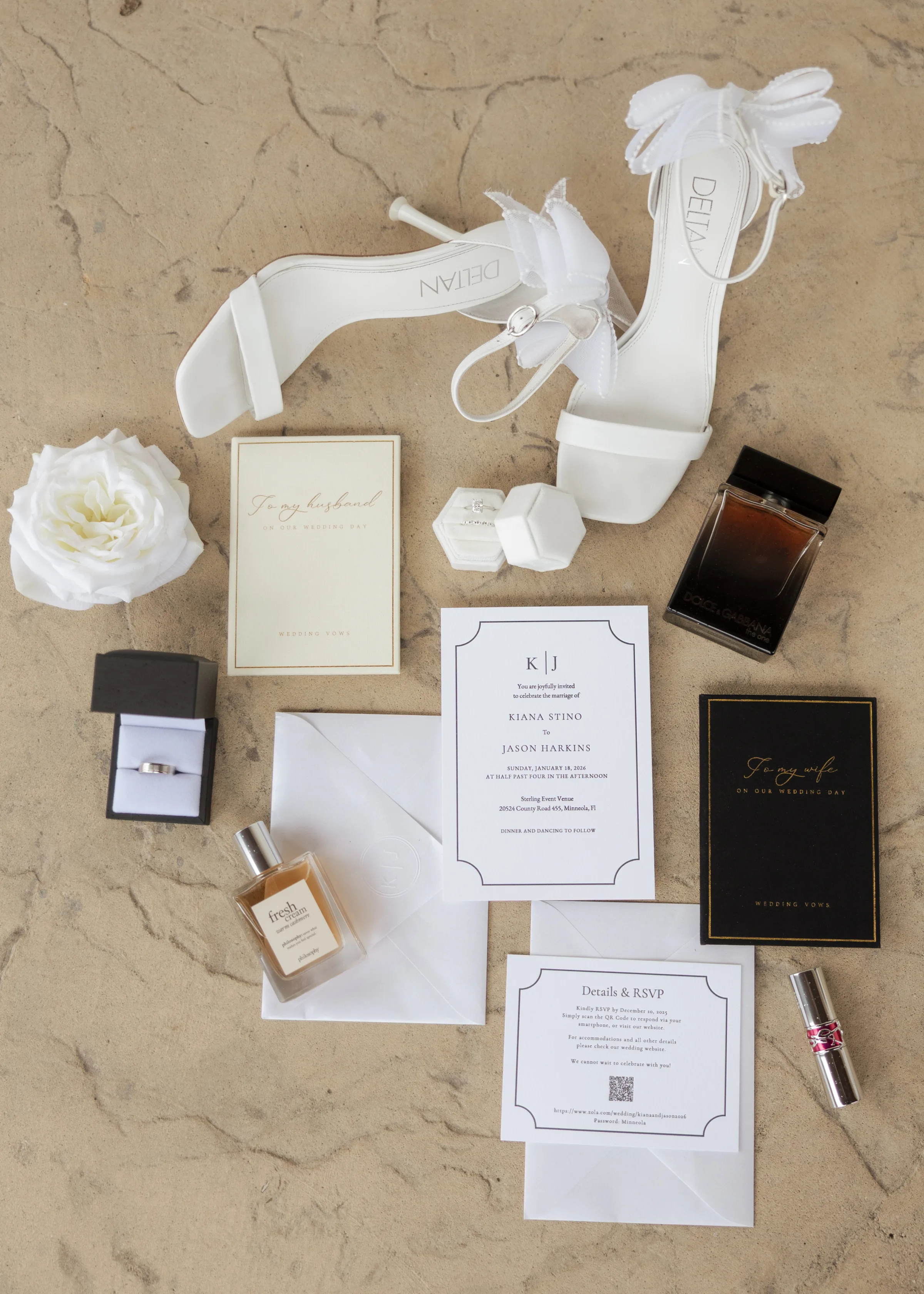 Wedding flat lay featuring white bridal heels by Dellian, Dolce and Gabbana cologne, Philosophy fresh cream perfume, wedding rings, white rose, lipstick, and elegant black and white wedding invitation suite for Kiana Stino and Jason Harkins at Sterling Event Venue in Minneola Florida