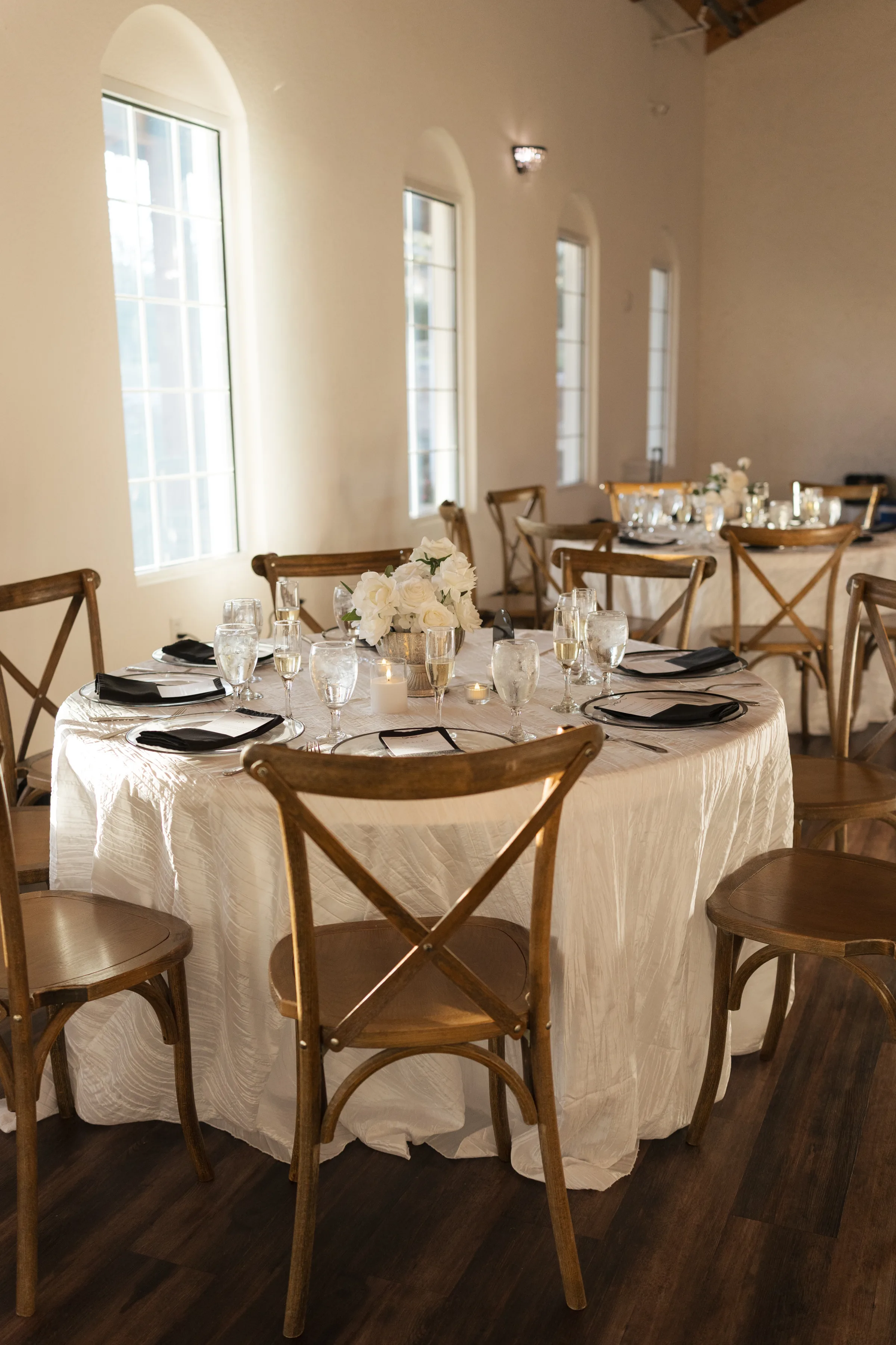 Elegant wedding reception table setting with white floral centerpiece, black napkins, and rustic crossback wooden chairs at a Central Florida wedding venue