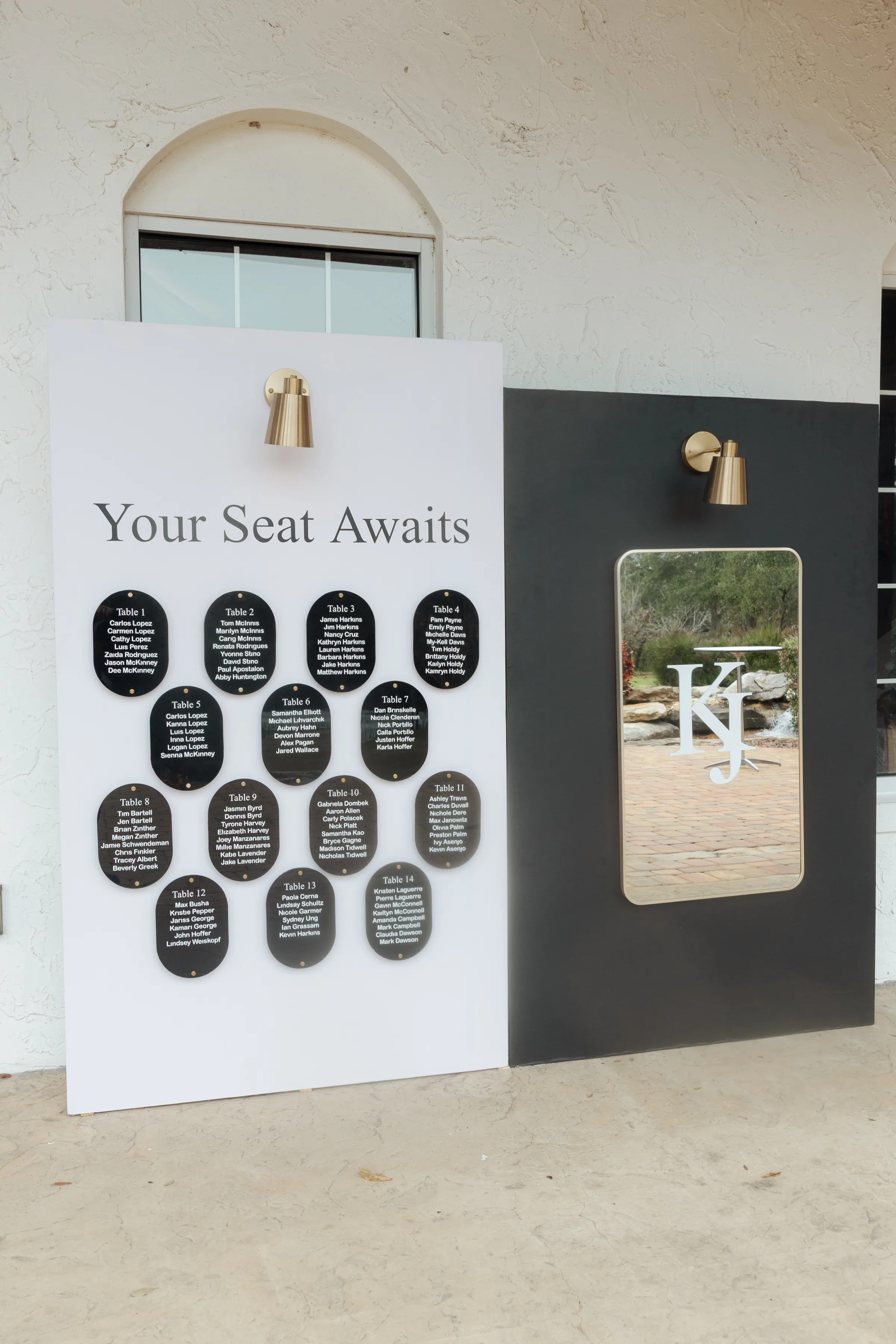 Elegant black and white wedding seating chart display reading Your Seat Awaits with oval table assignment plaques and monogram mirror sign at a Central Florida wedding venue