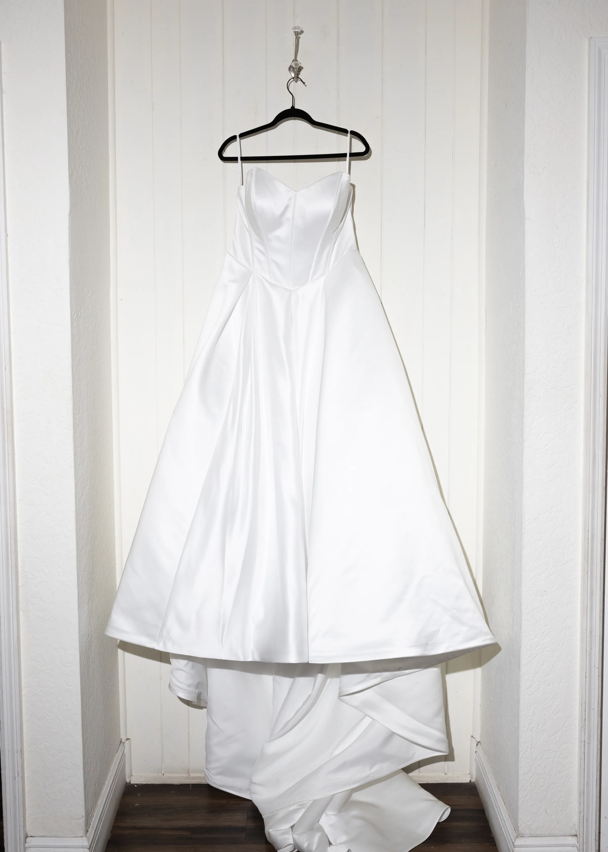 White satin strapless ballgown wedding dress with cathedral train hanging on black hanger against white wall in Orlando Florida bridal suite